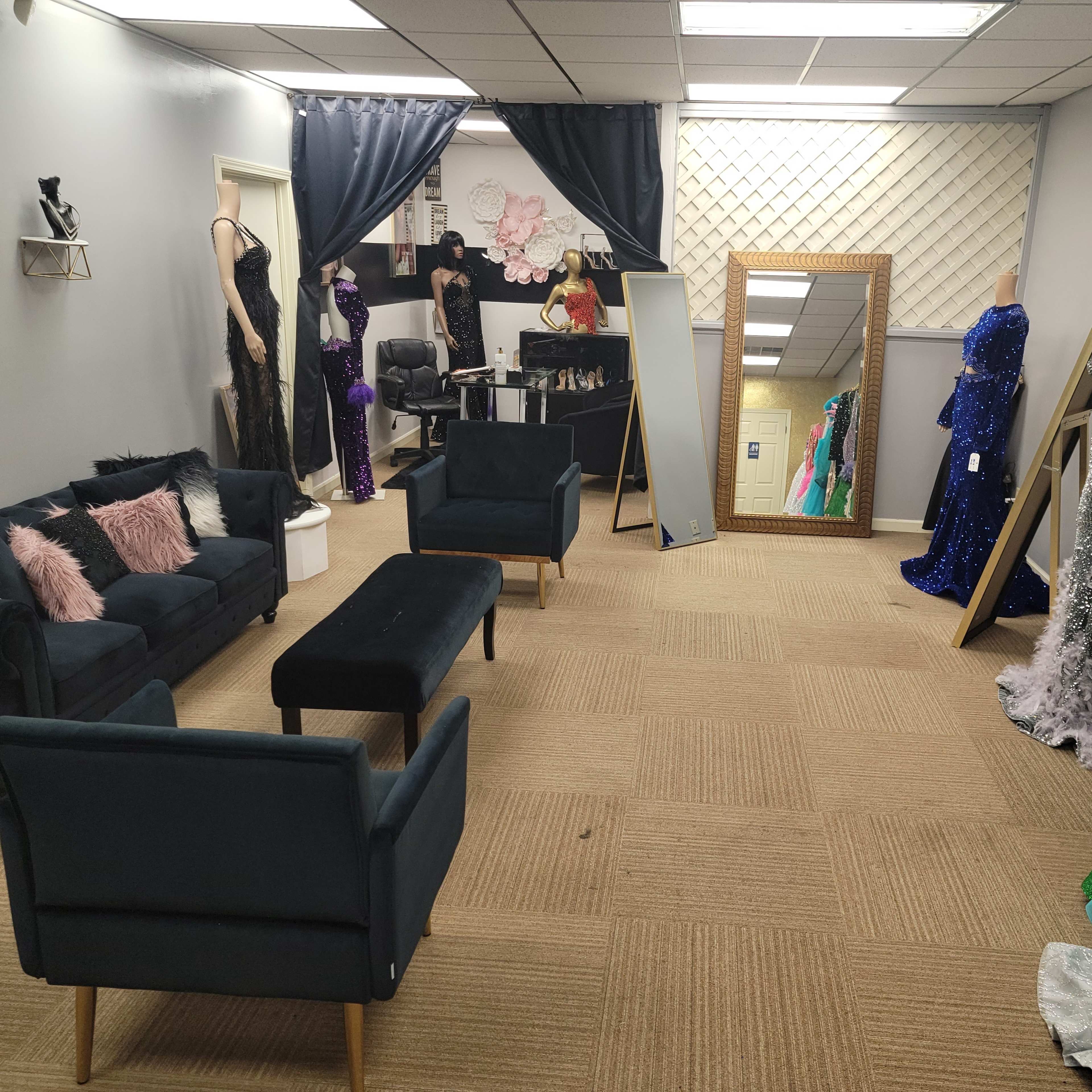 A boutique interior with dark green sofas, a mirror, and various formal dresses displayed on racks and mannequins.