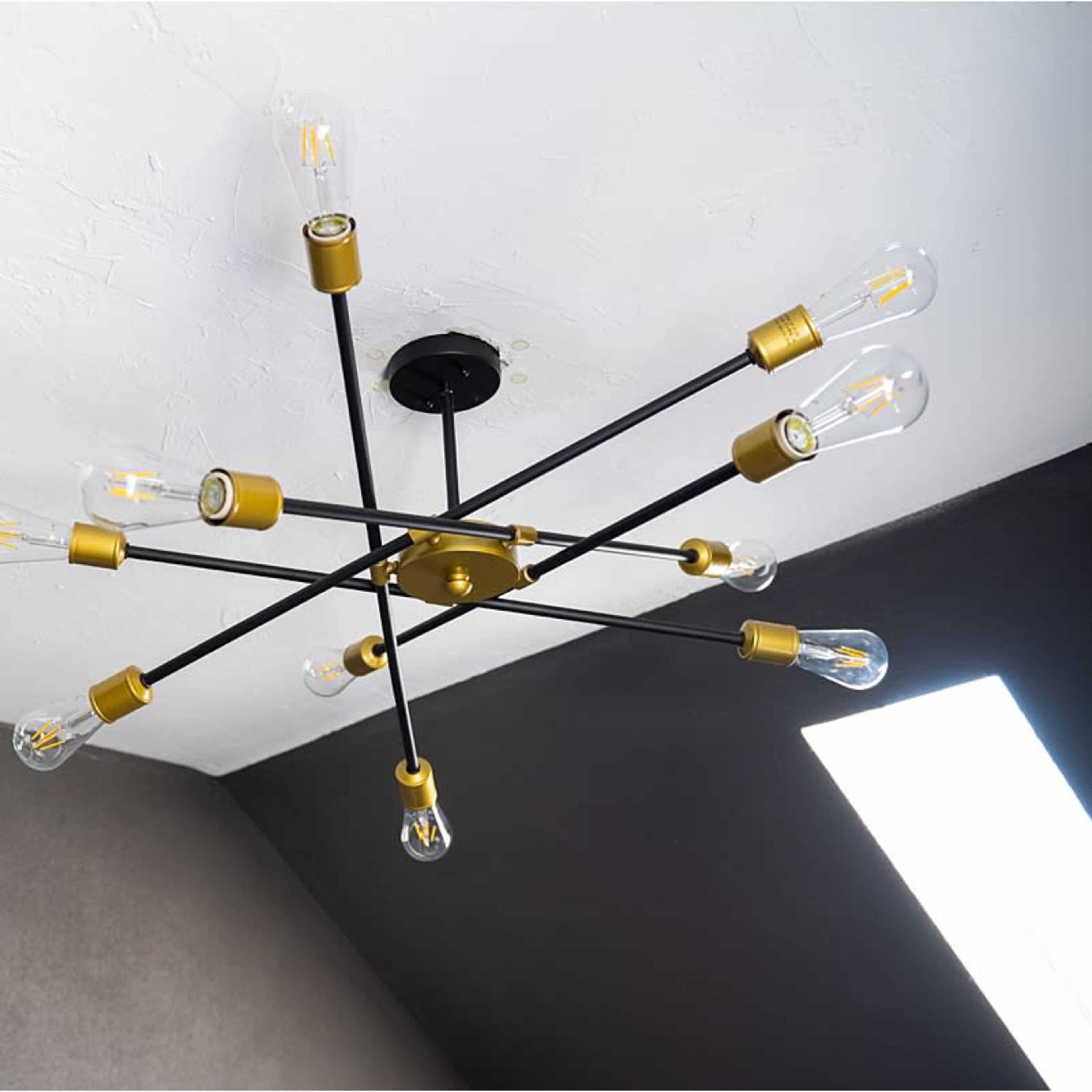 A modern chandelier with multiple light bulbs is mounted on a ceiling, contrasting with the dark wall.