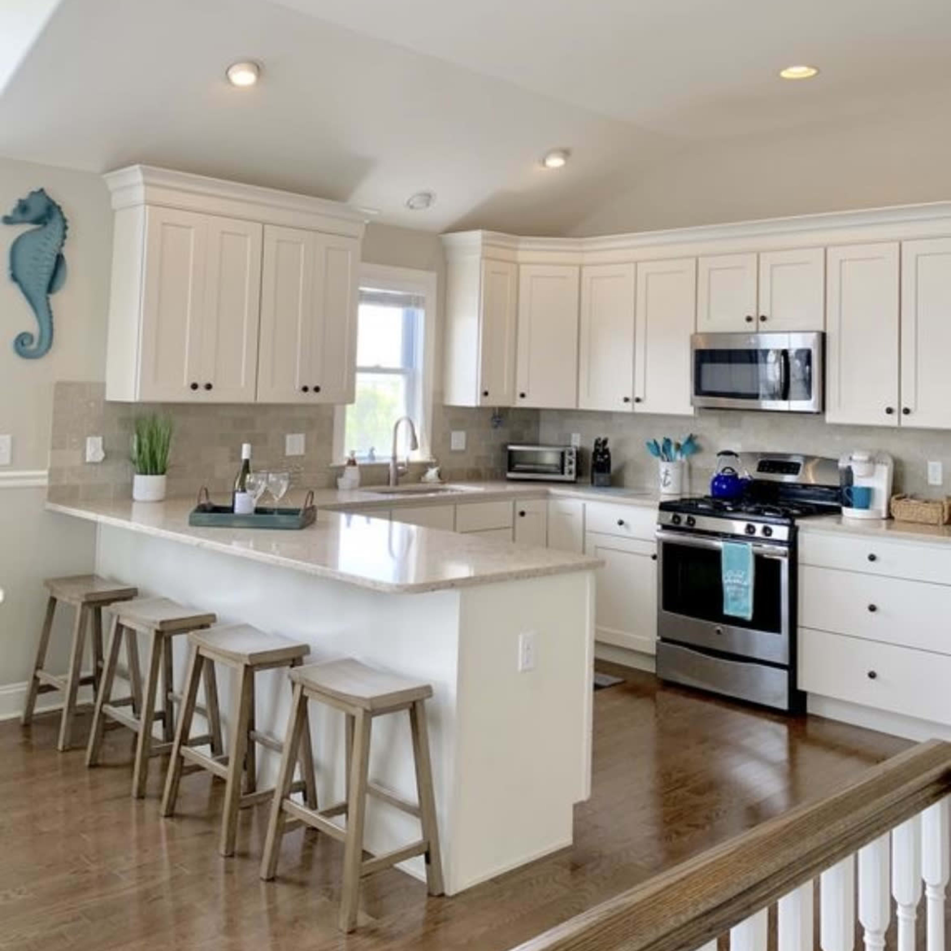A modern kitchen features white cabinetry, stainless steel appliances, and a central island with seating for three.