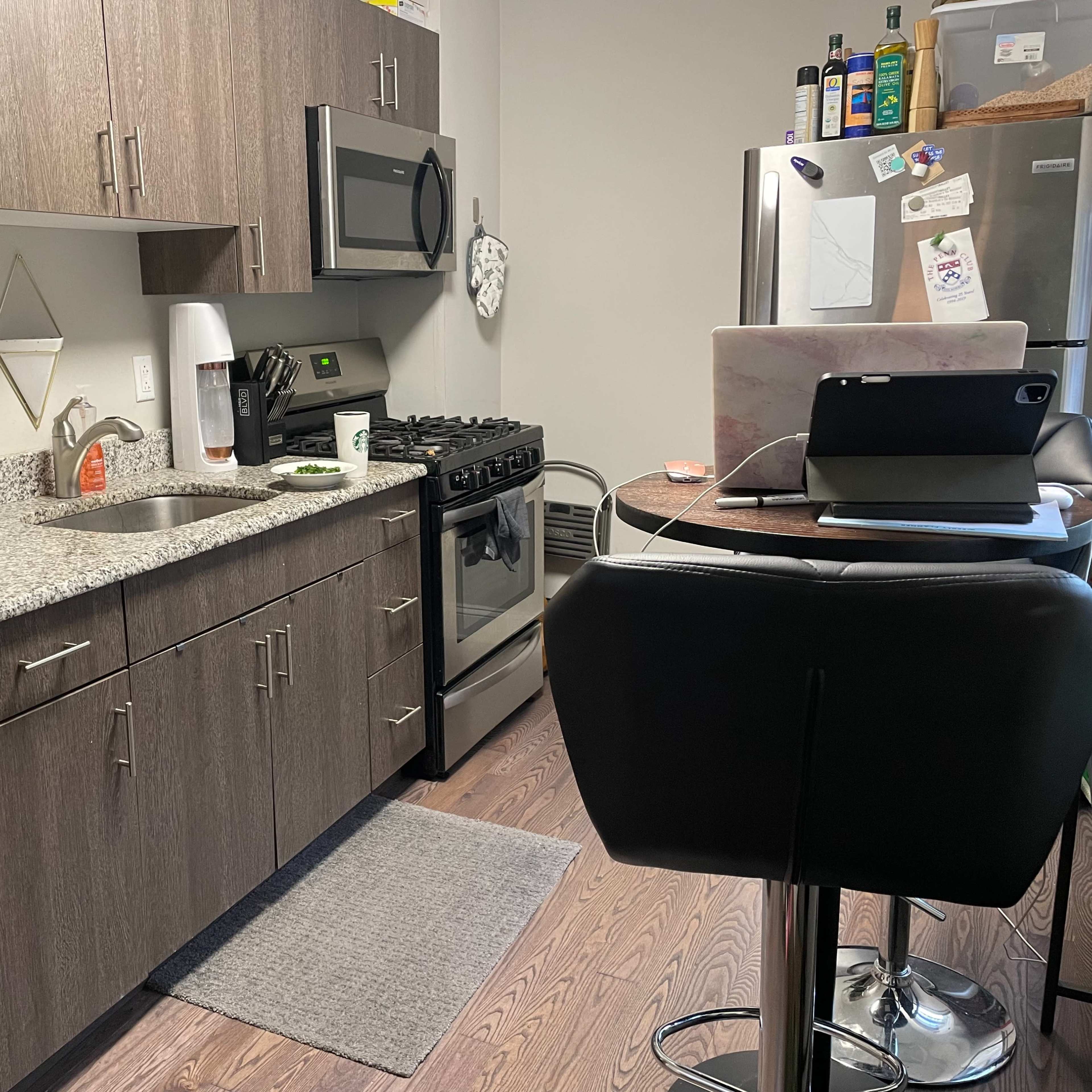A modern kitchen with wooden cabinetry, stainless steel appliances, and a small dining table with a laptop on it.