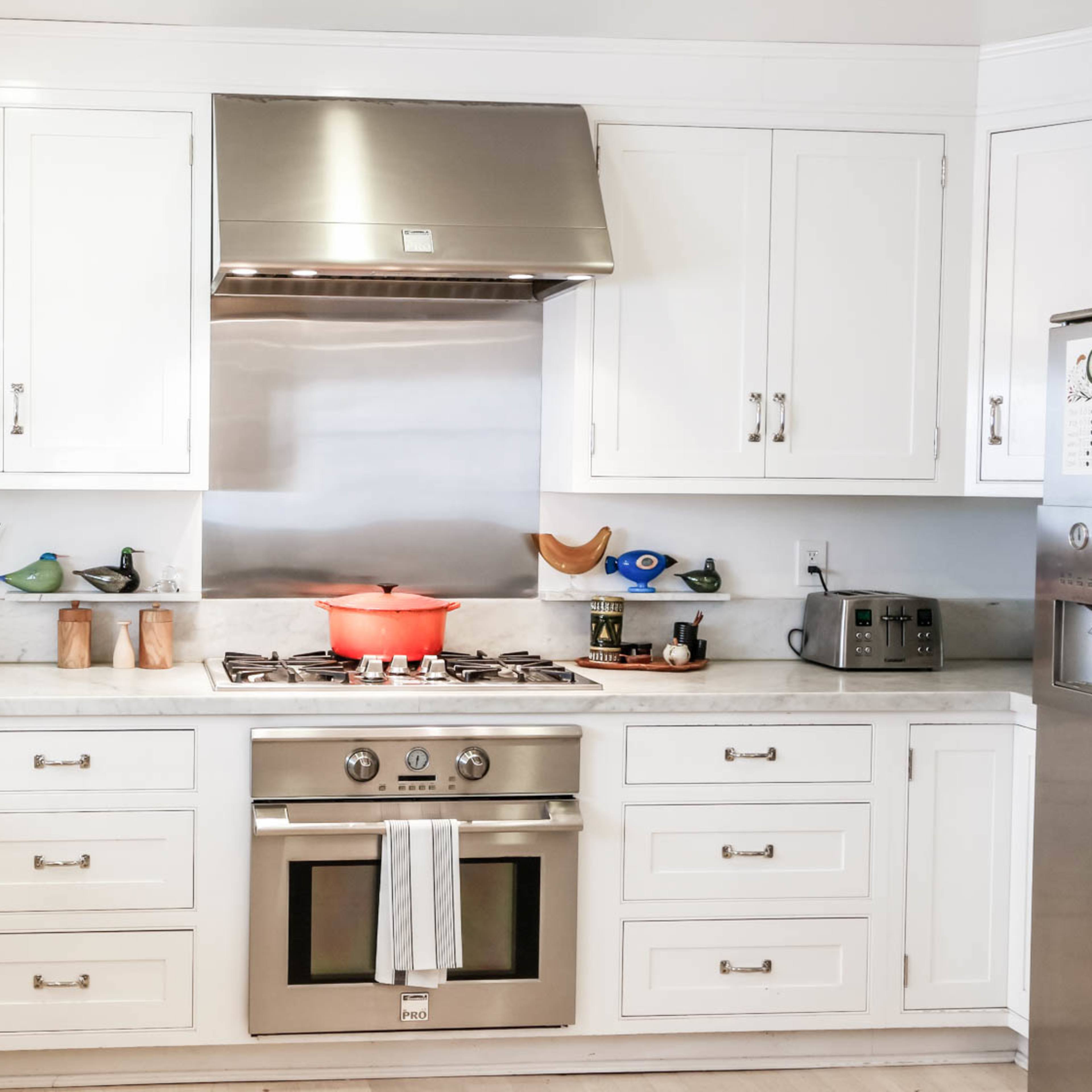 A modern kitchen features white cabinetry, a stainless steel stove, and a central island with various kitchen appliances and decor.