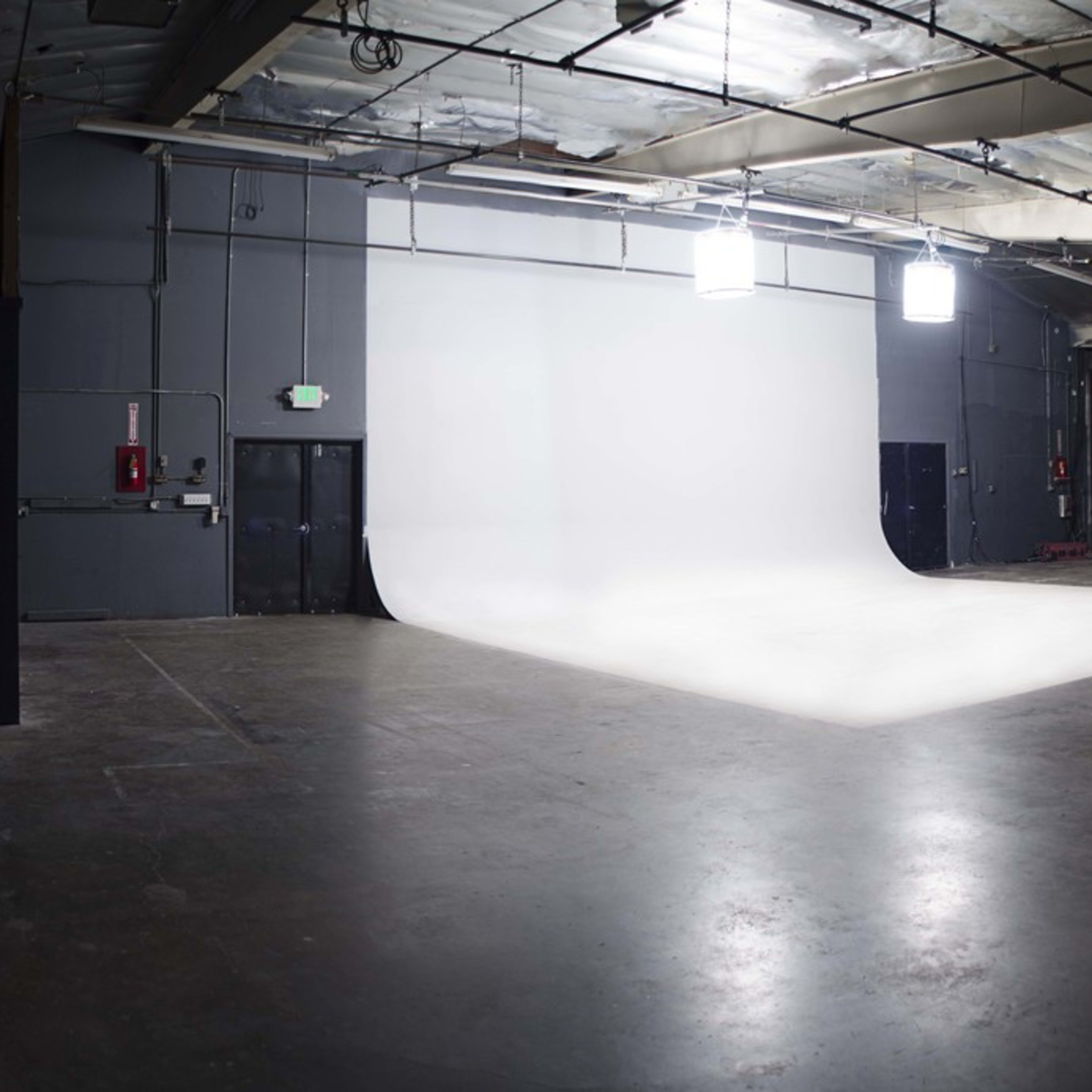A spacious photo studio with a seamless white backdrop, concrete floors, and overhead lighting.