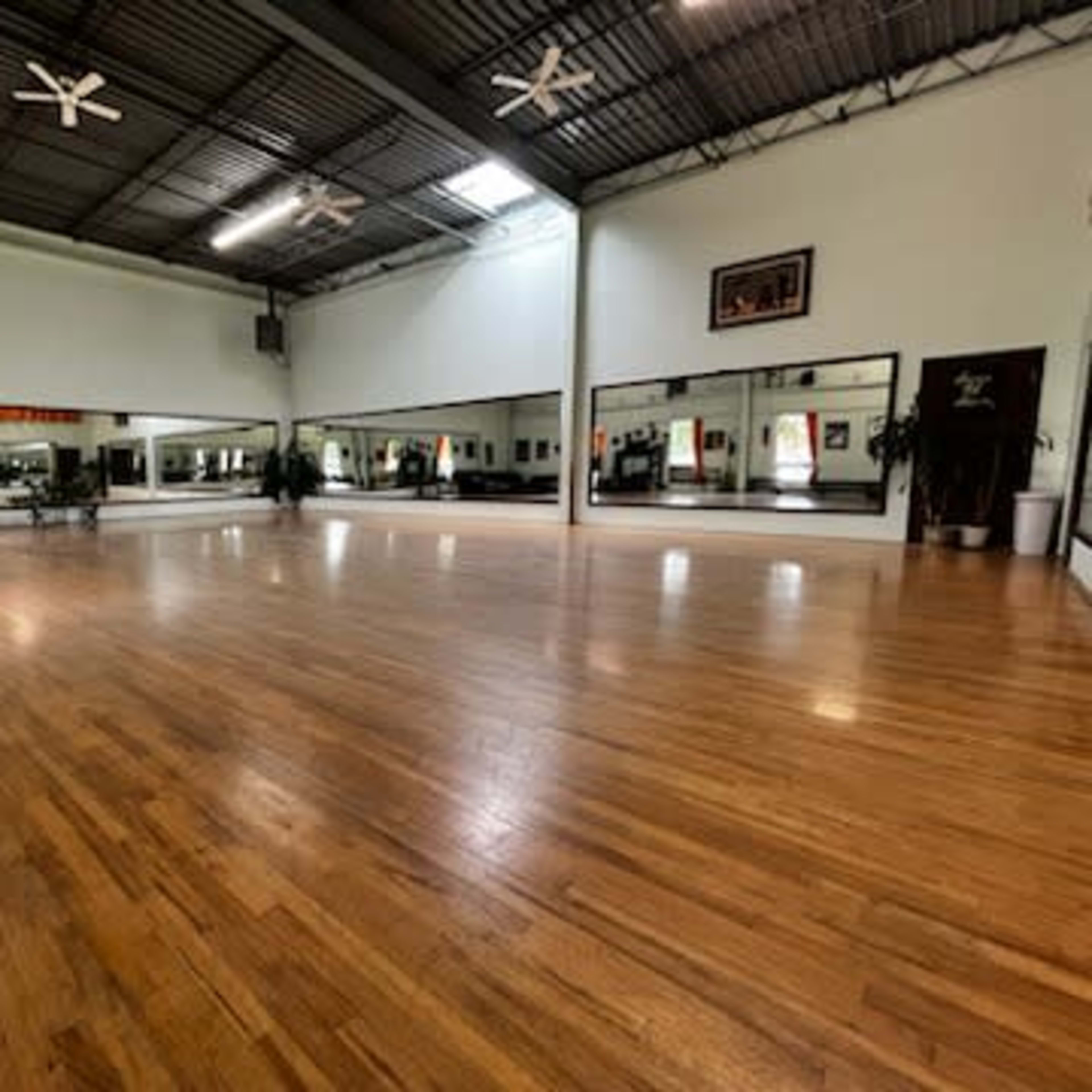 A spacious dance studio with wooden flooring and large mirrors on the walls.