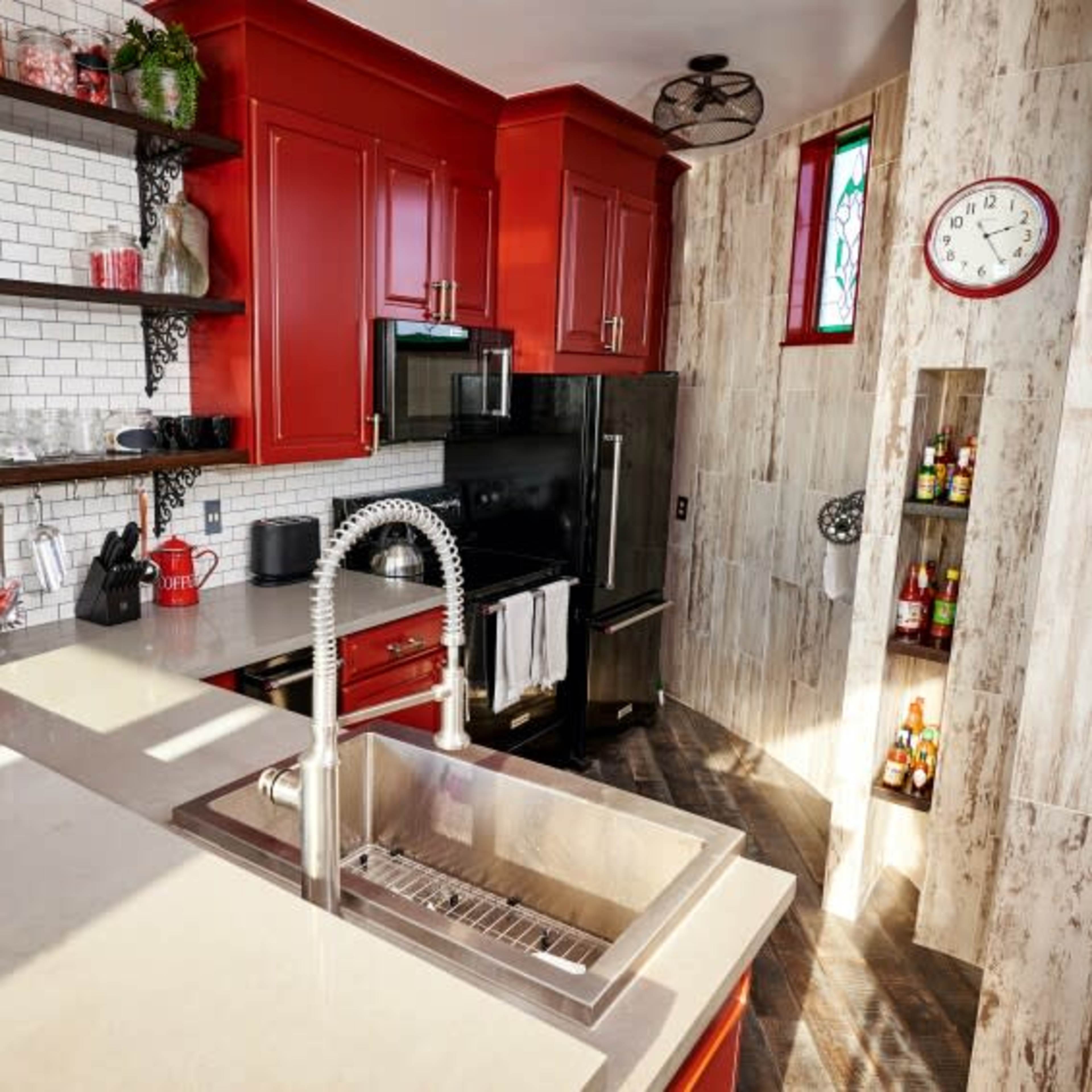 A modern kitchen with red cabinets, a stainless steel refrigerator, and a gray countertop featuring a sink.