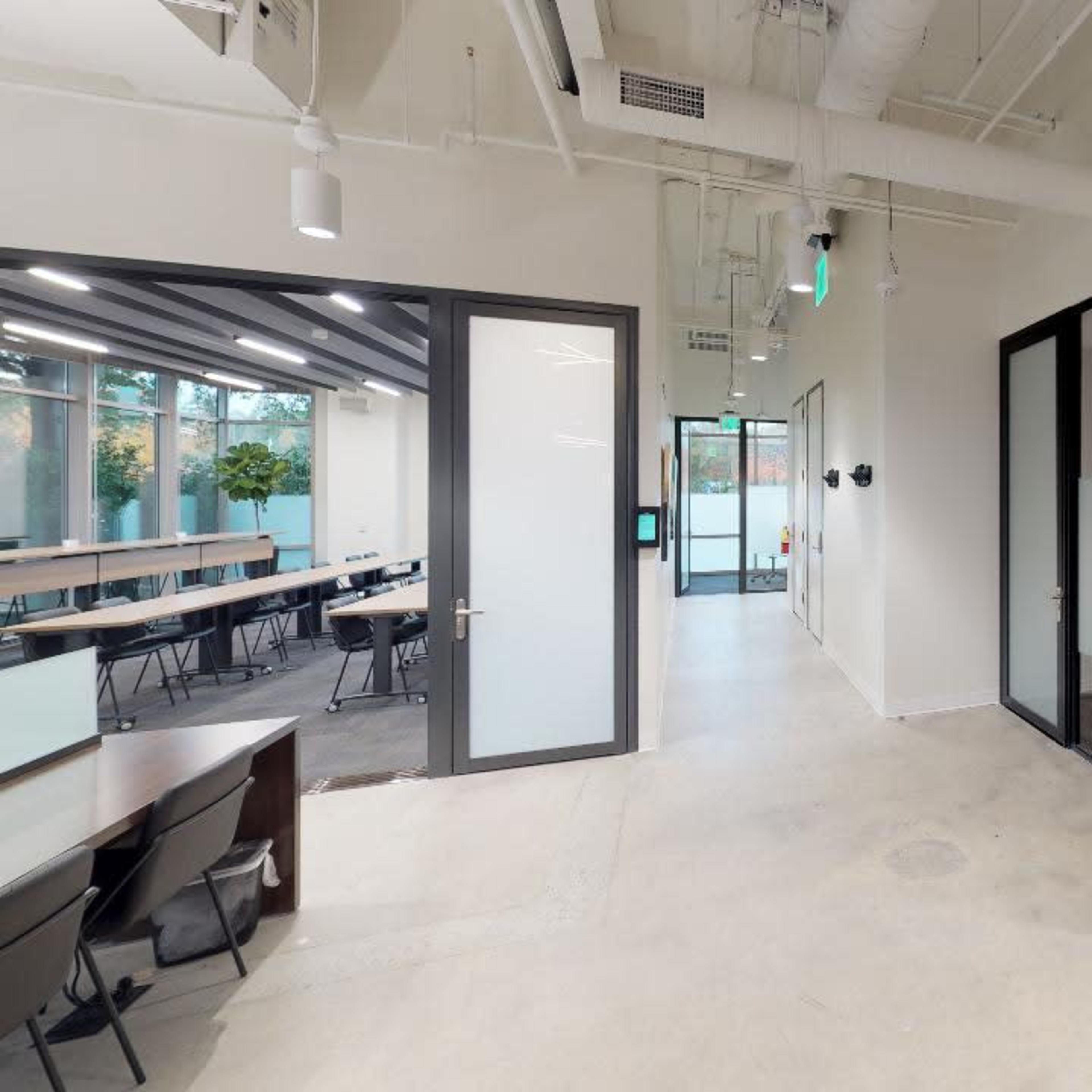 A modern office interior with glass-walled meeting rooms, a kitchenette area, and open workspace.