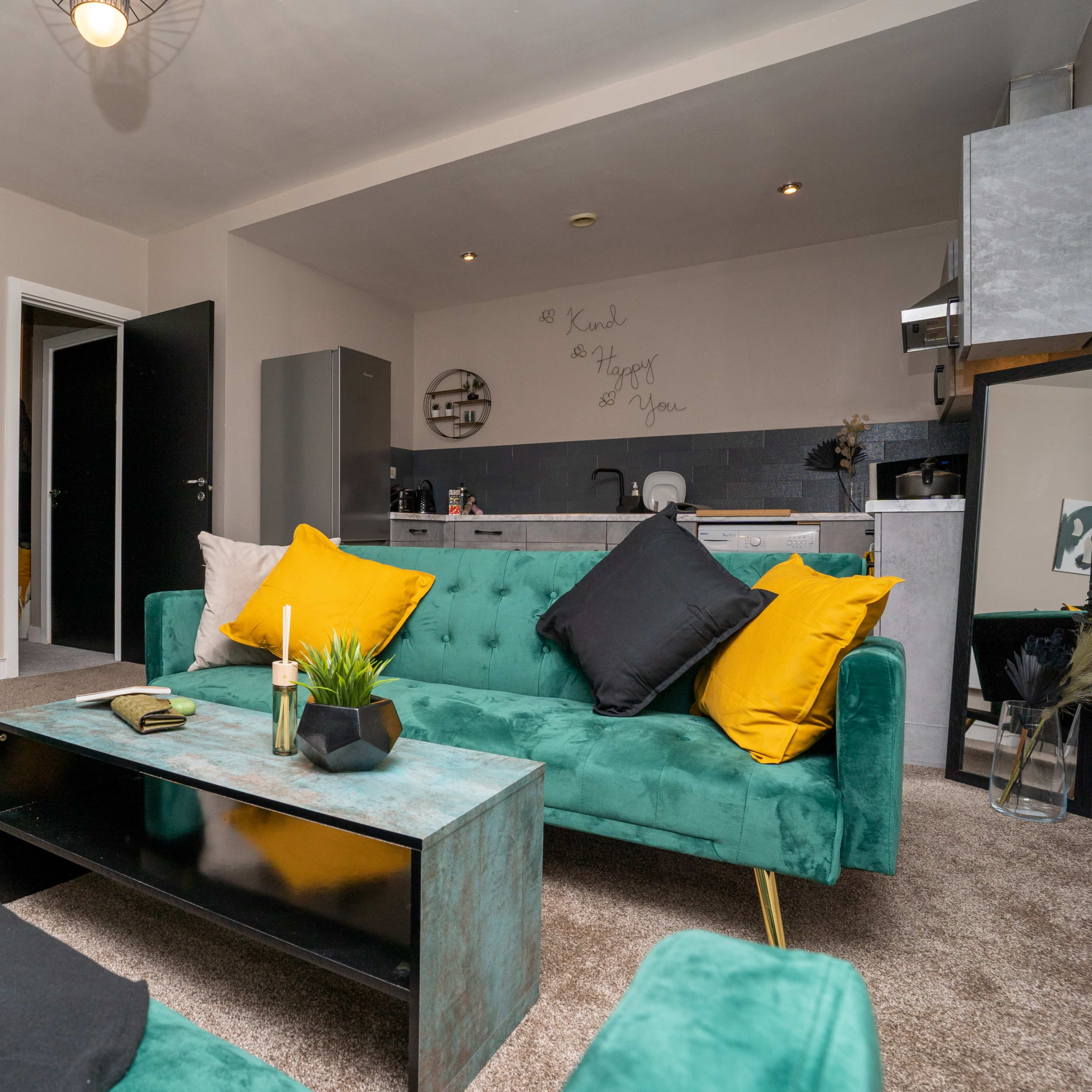 A cozy living room with teal sofas, a black coffee table, and an adjoining kitchen area.