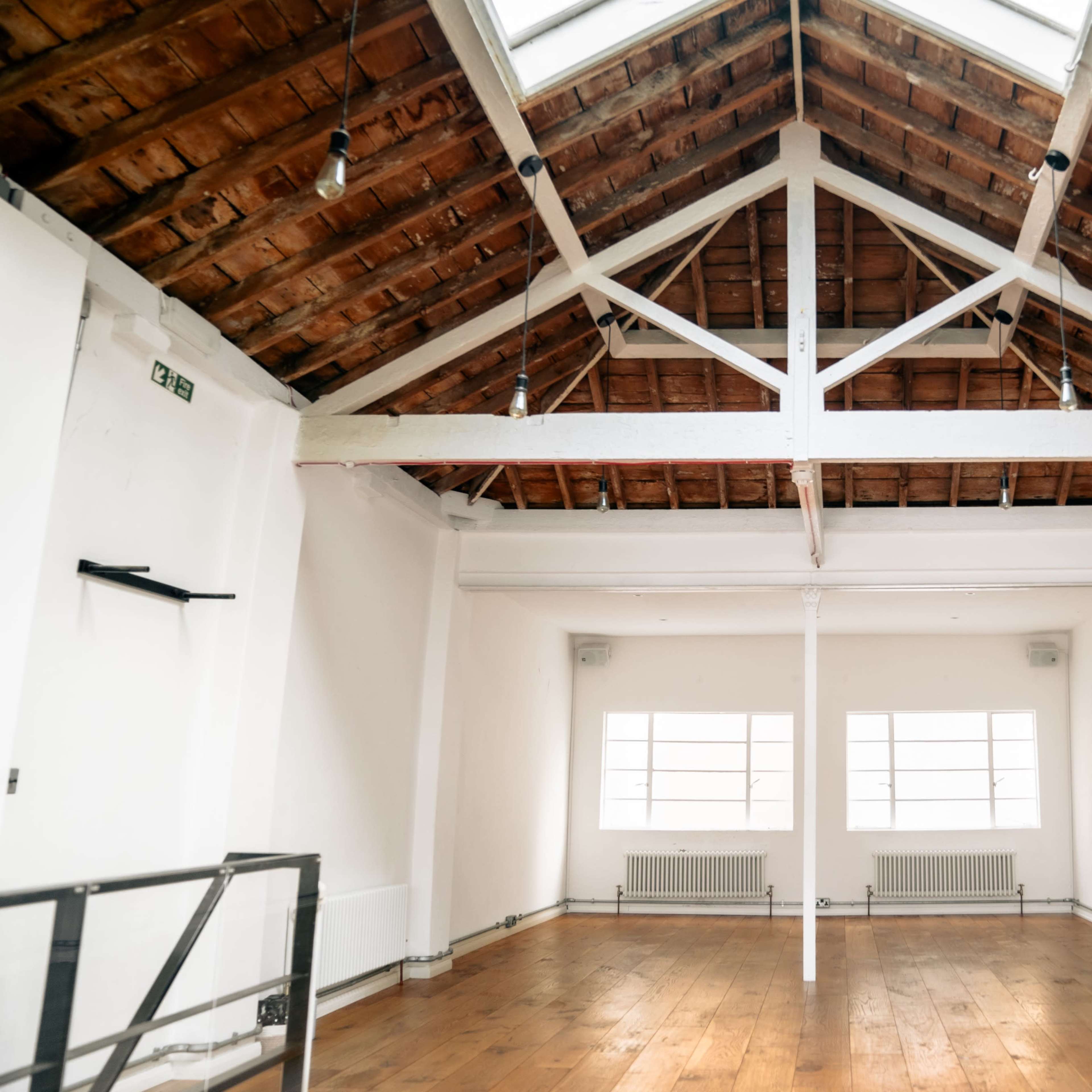 A spacious room with a high, wooden-beamed ceiling and large windows allowing natural light to enter.