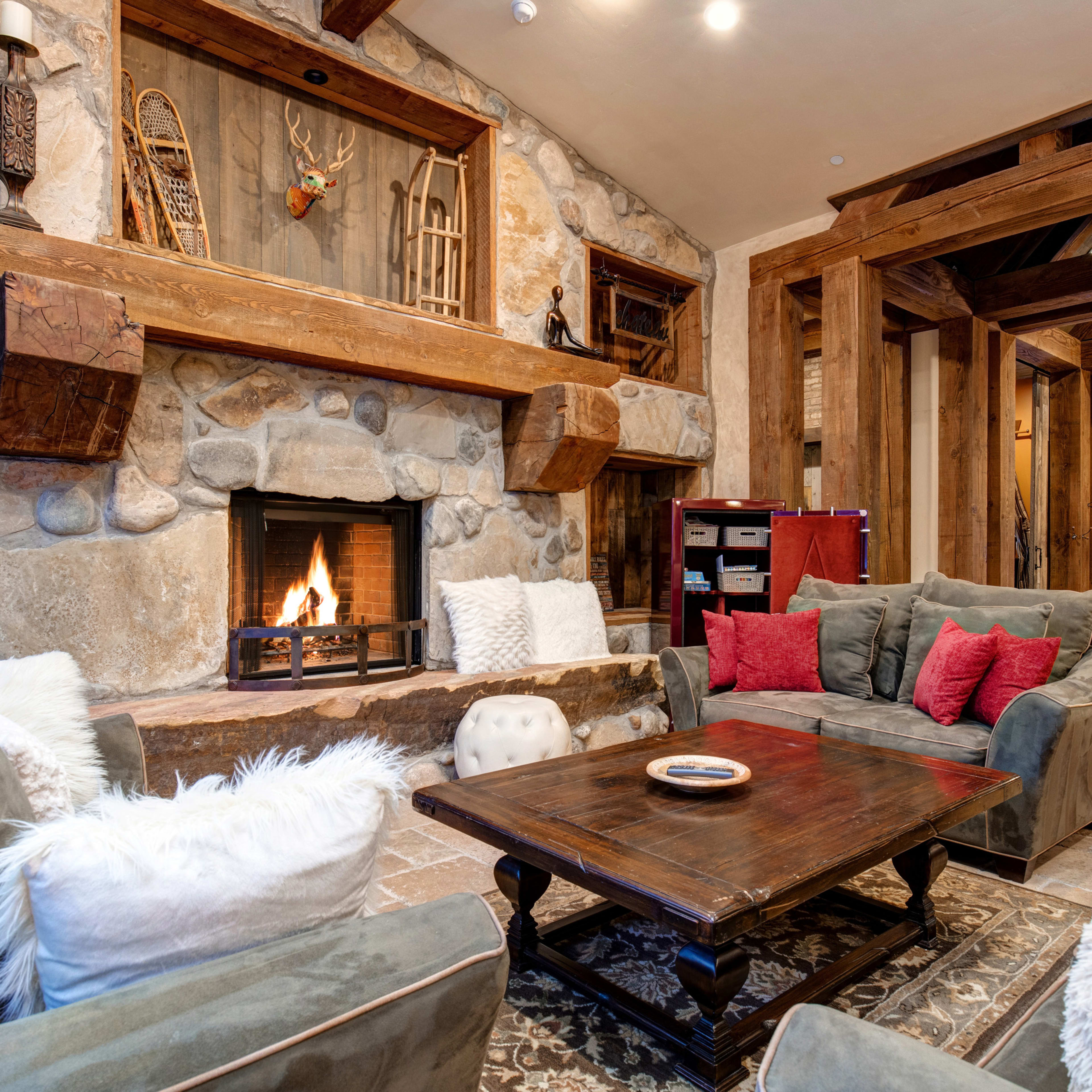A cozy living room features a stone fireplace surrounded by comfortable seating and rustic wooden beams.