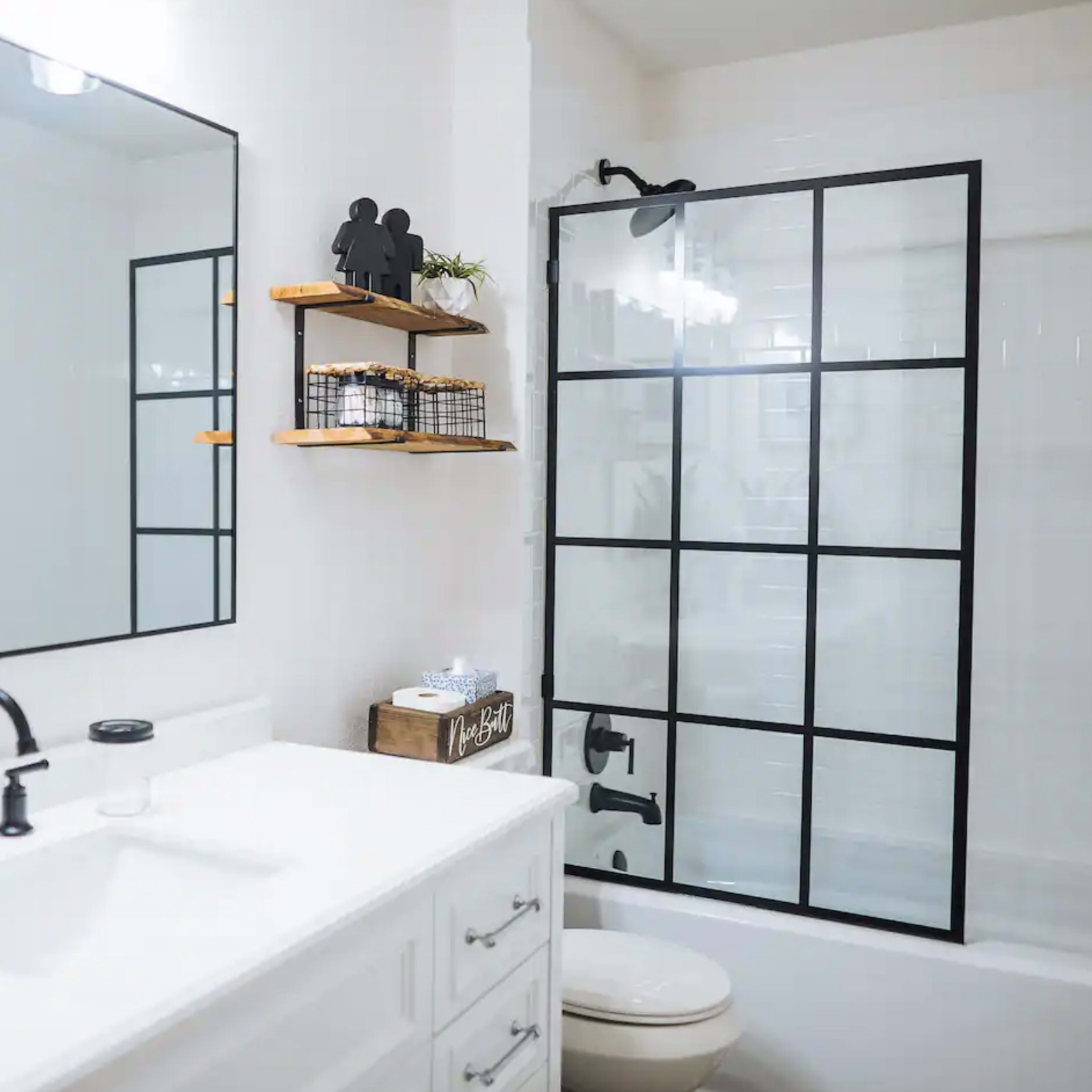 A modern bathroom featuring a white vanity with a black faucet, a large mirror, and a shower with a black framed glass door.