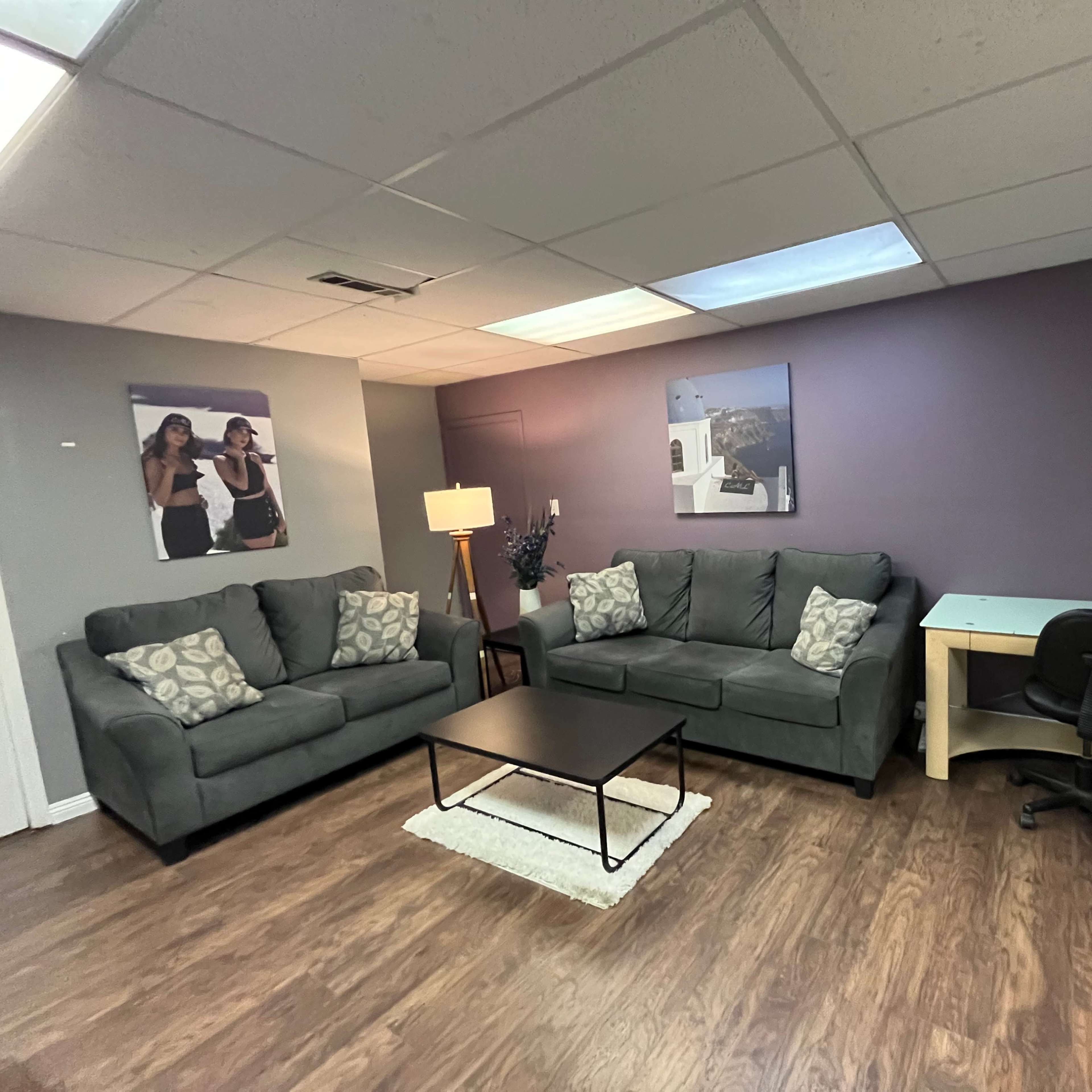 A cozy waiting area with two gray sofas, a coffee table, a desk with a chair, and framed pictures on the wall.
