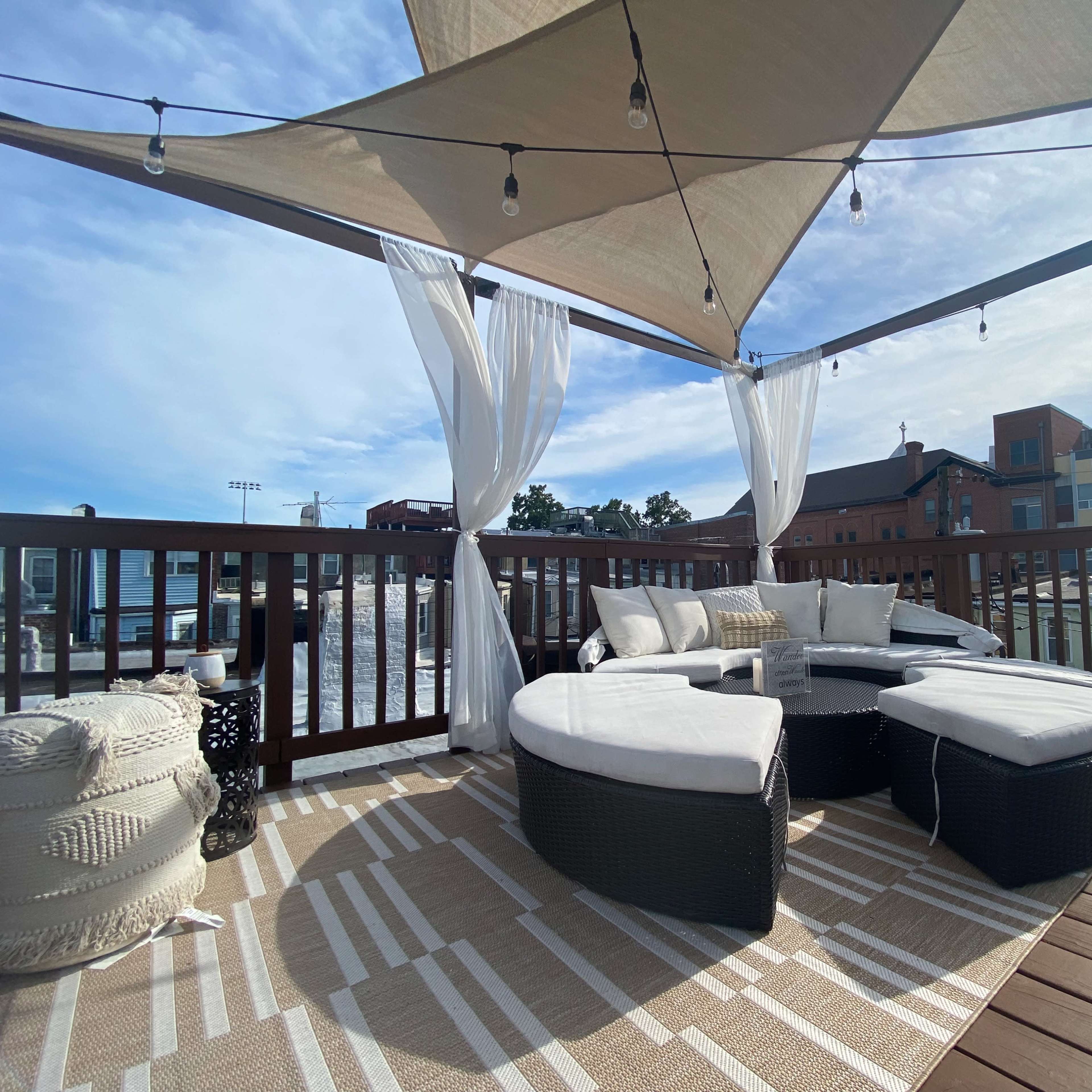 A shaded outdoor sitting area features rattan furniture and curtains on a wooden deck.