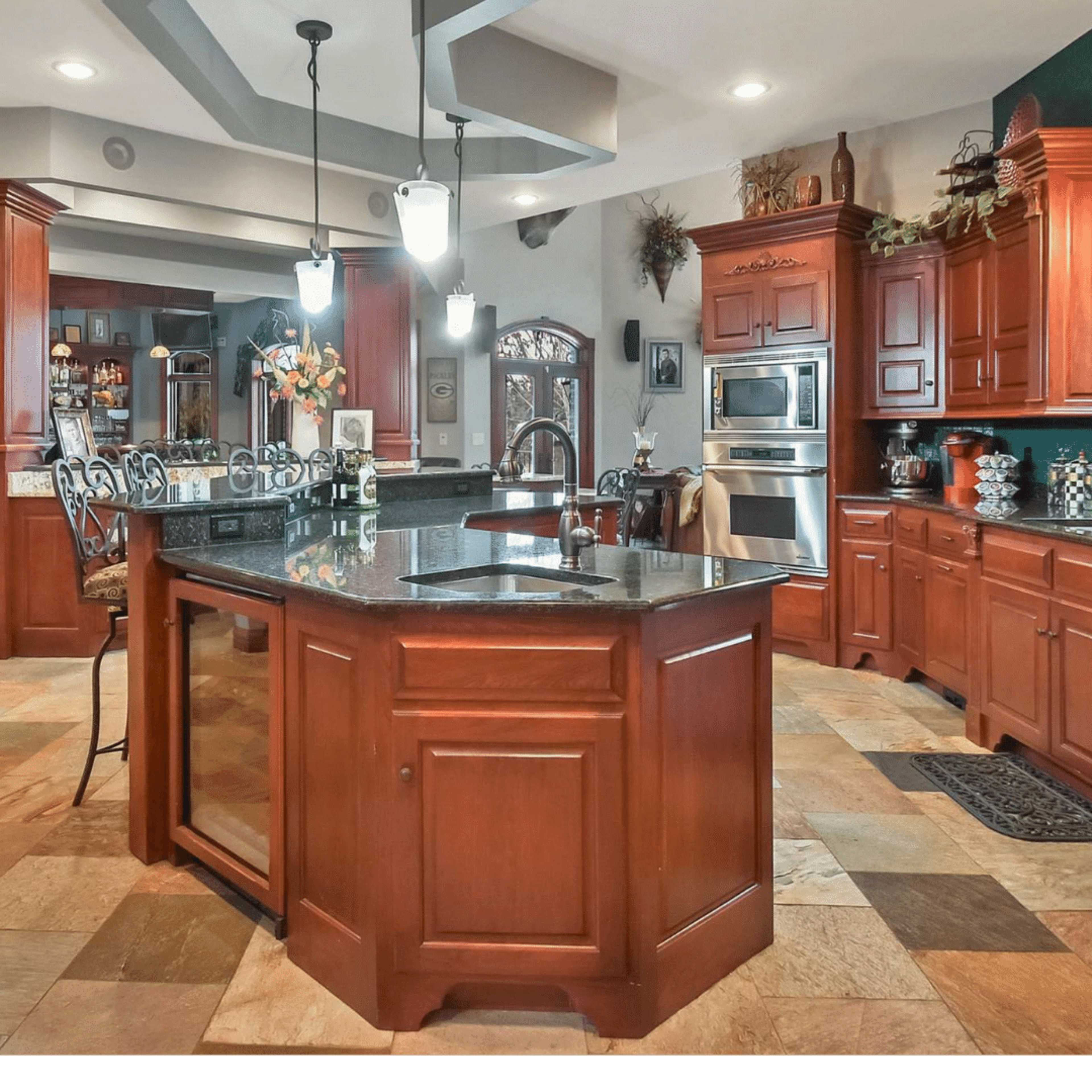 A spacious kitchen featuring dark wood cabinetry, a large central island with a black countertop, and a tiled floor.