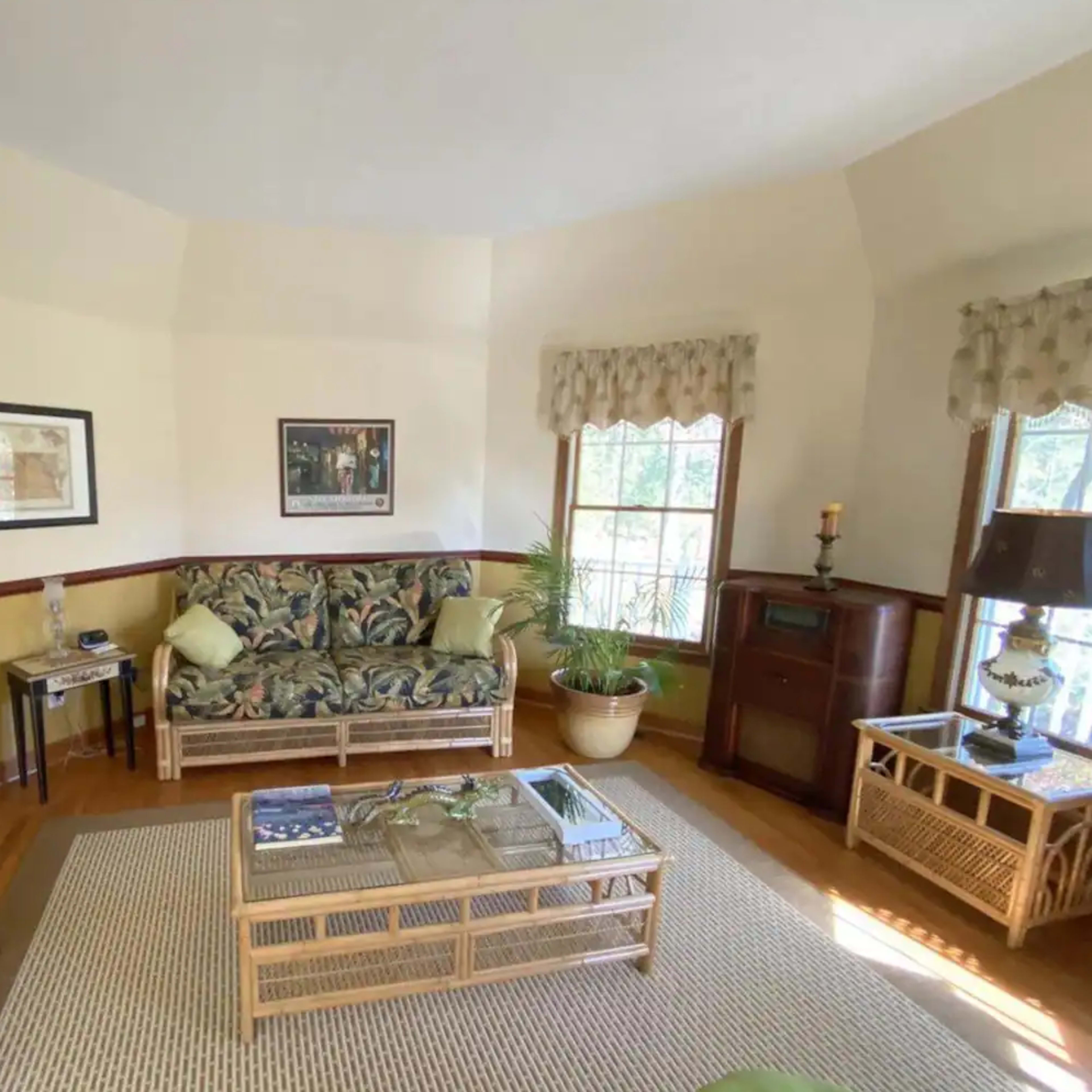 A living room with two floral-patterned sofas, a coffee table, and a window with light curtains.