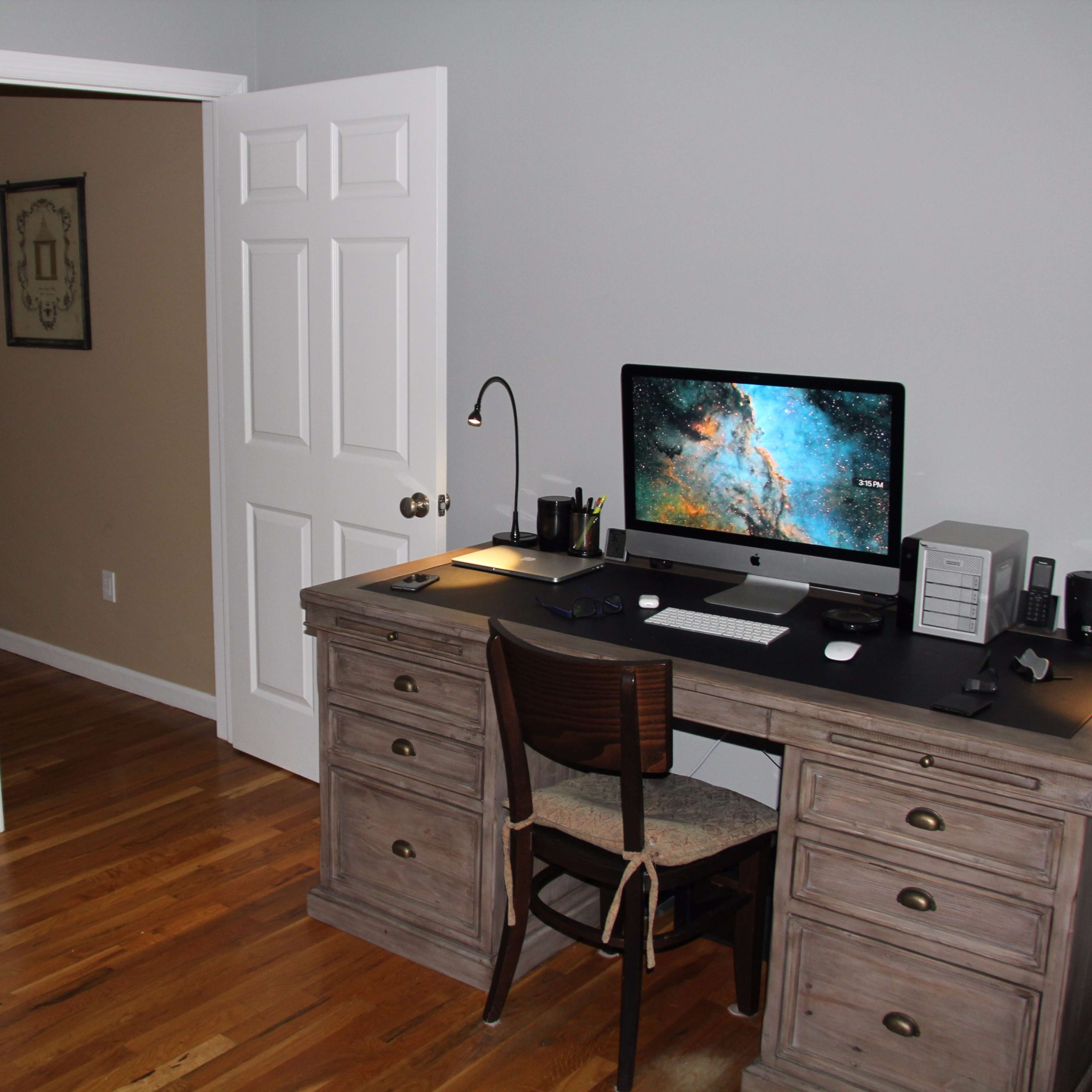 A simple office setup features a wooden desk with a computer and a chair, adjacent to an open door leading to another room.