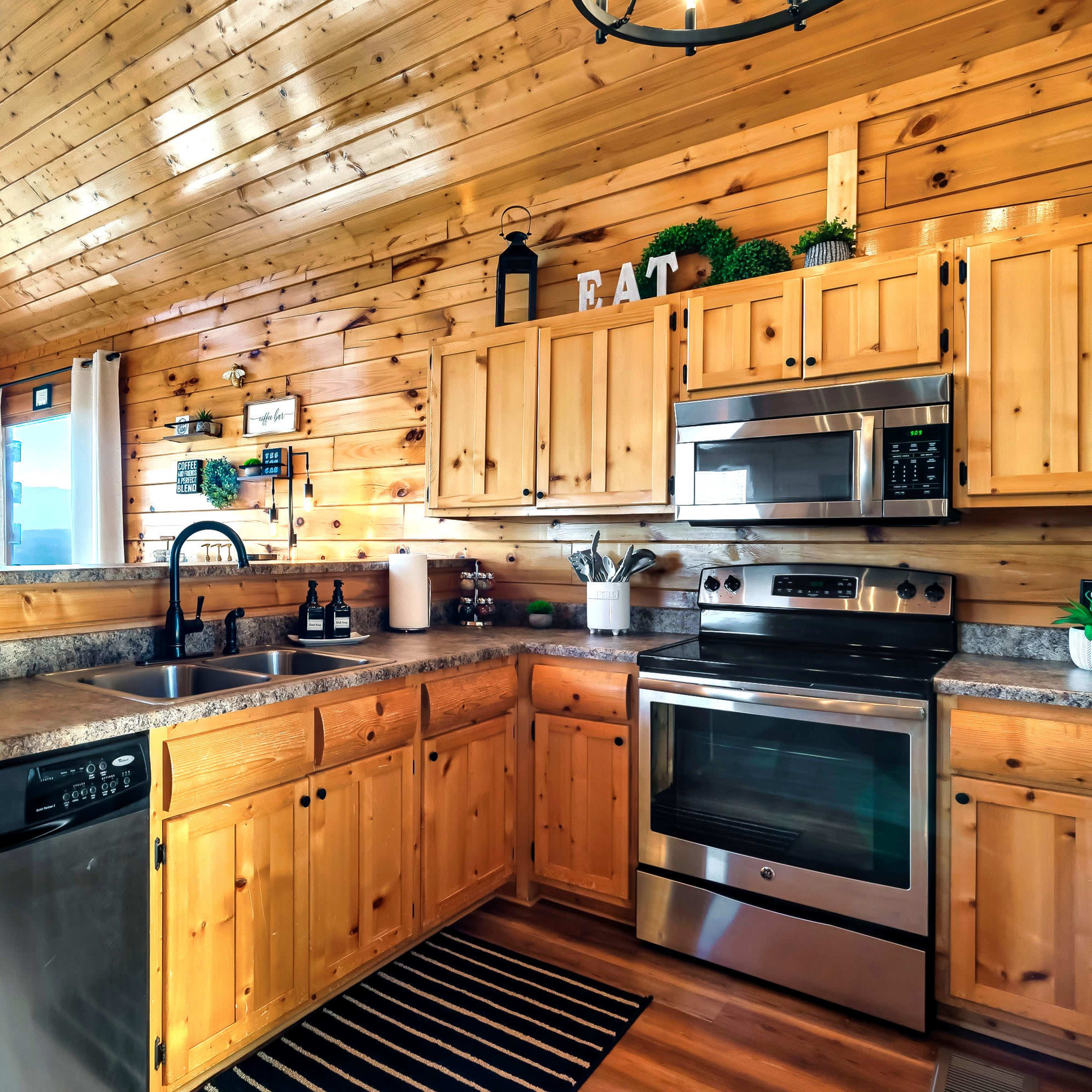 A wooden kitchen with a high ceiling, featuring stainless steel appliances, a stone countertop, and wooden cabinetry.