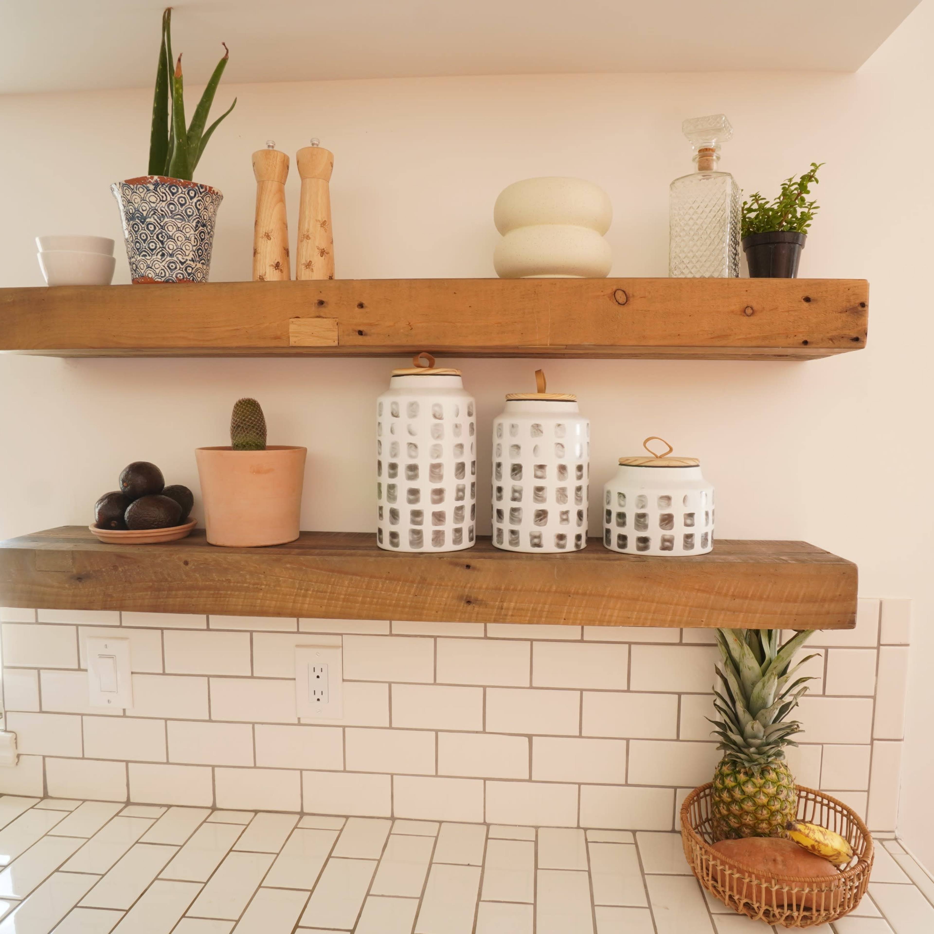 A kitchen area with wooden shelves displaying potted plants, ceramic jars, and a pineapple on a tiled countertop.