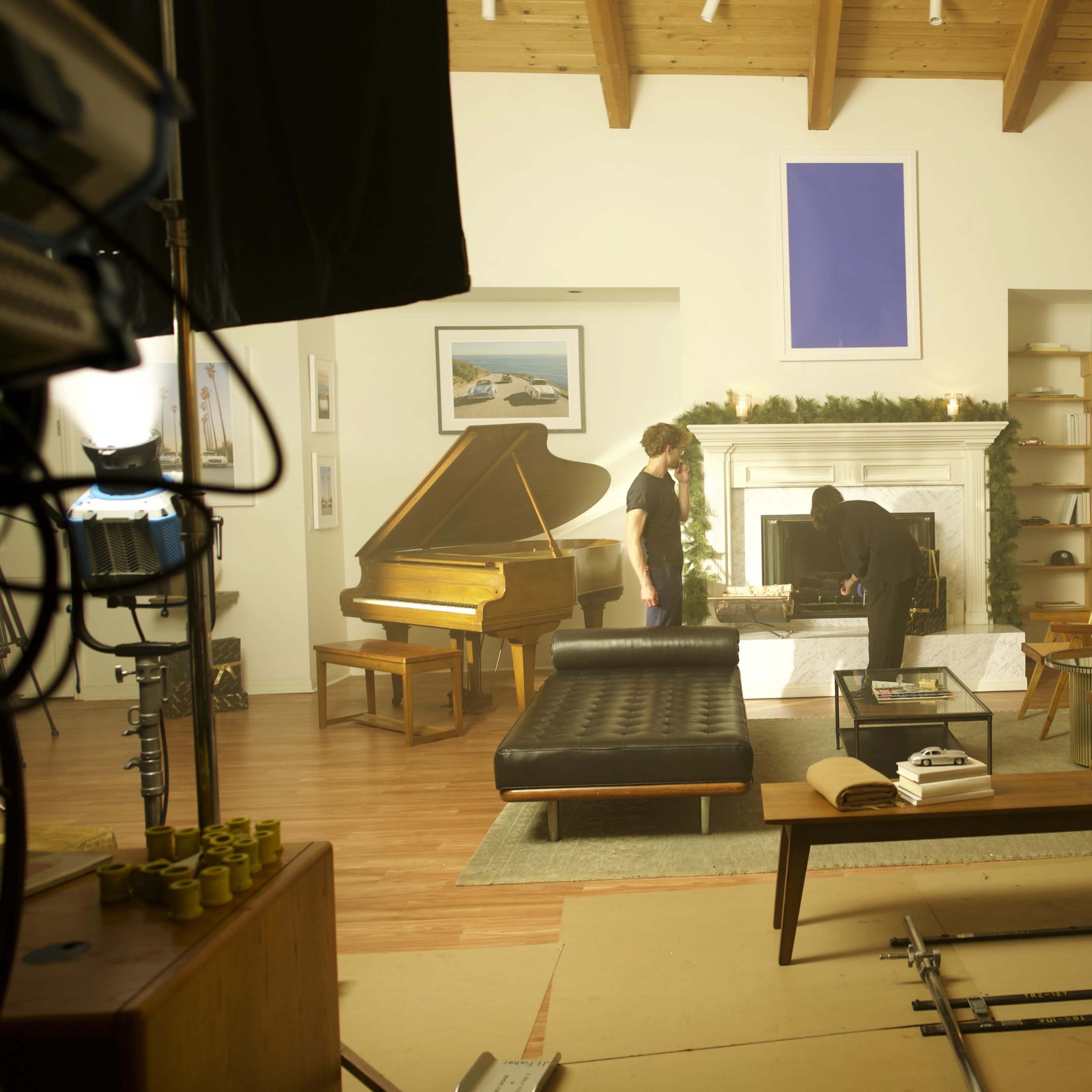 A living room scene features a grand piano, a decorated Christmas tree, and modern furniture, with two individuals engaged in activity near the fireplace.