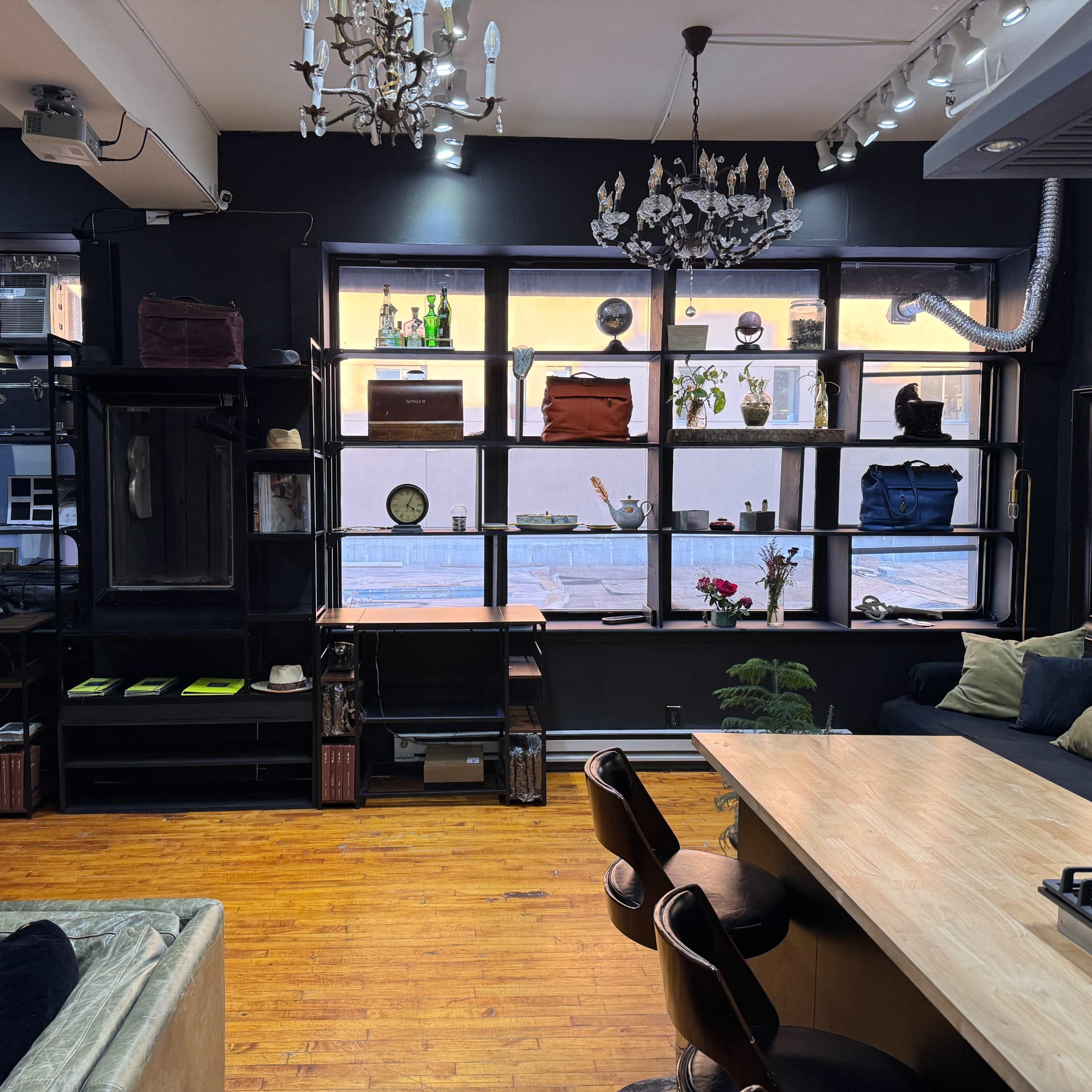 A stylish interior of a cafe or shop featuring large windows, shelves displaying various items, a wooden table, and seating.