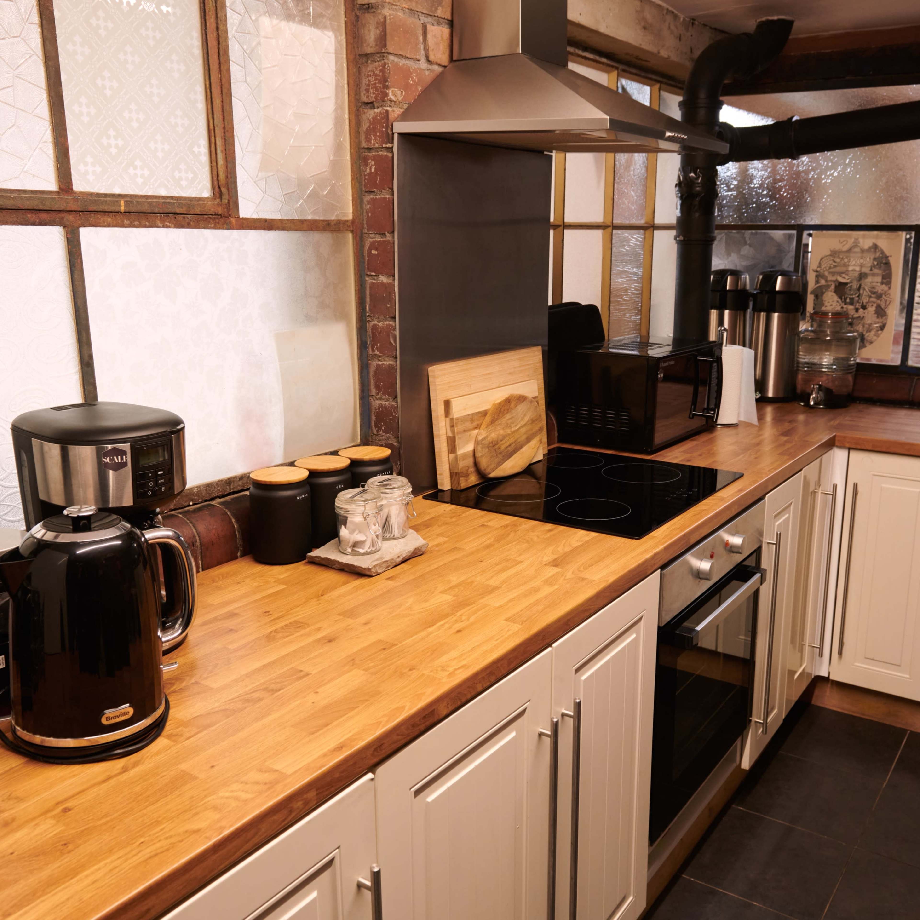 A modern kitchen featuring wood countertops, black appliances, and a metal exhaust hood.