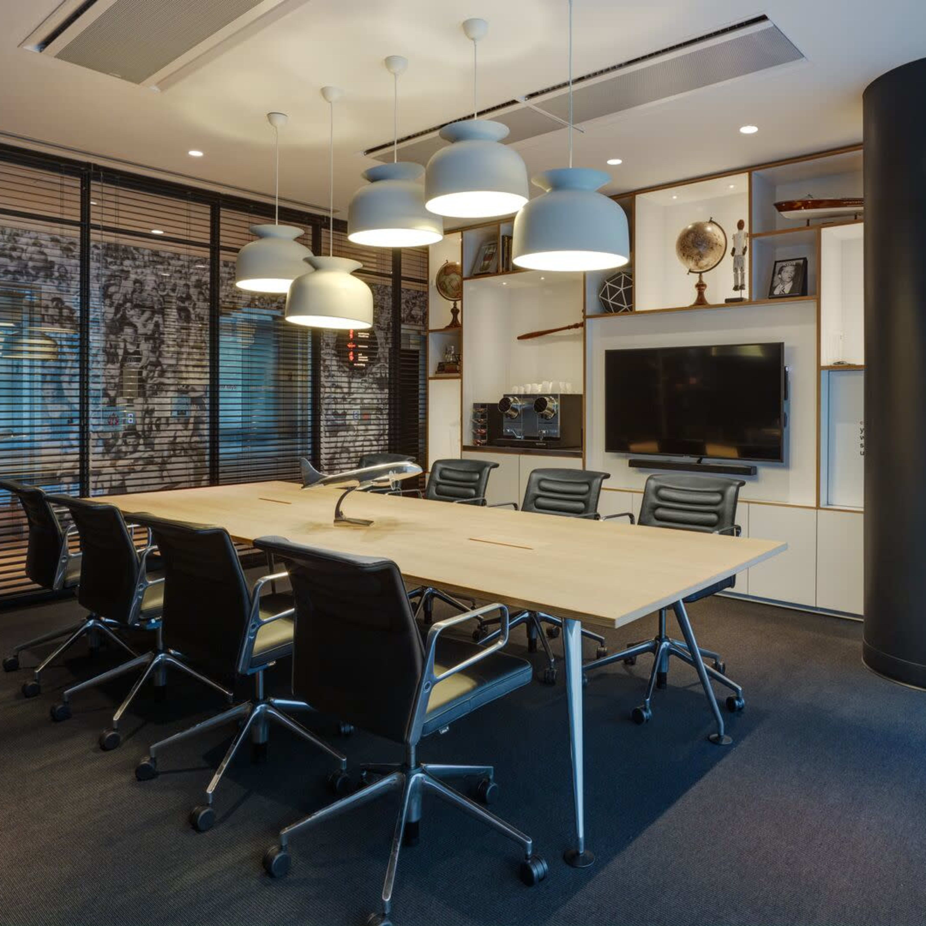A modern conference room features a large table surrounded by black chairs, with pendant lights overhead and a wall adorned with framed artwork.
