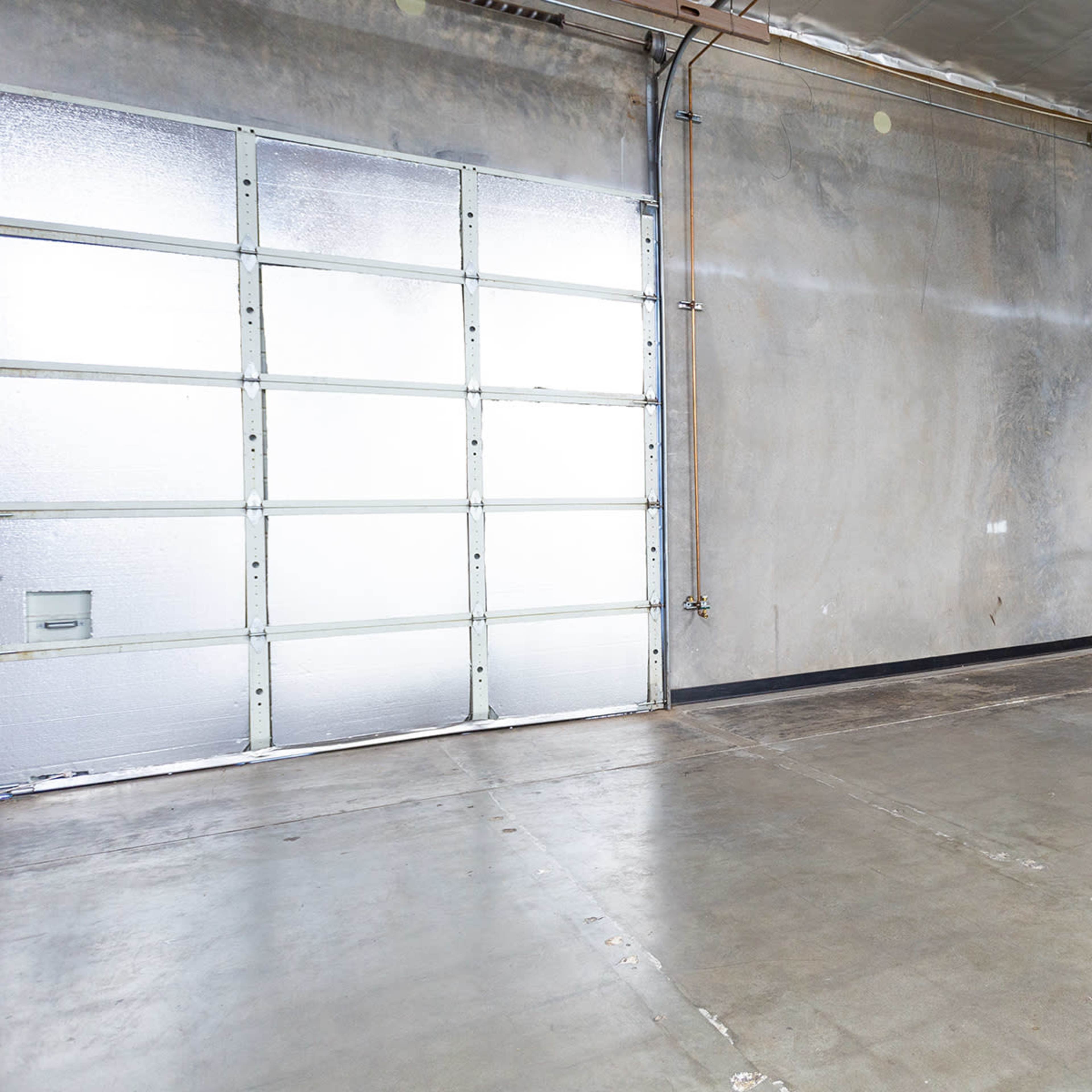 A spacious, empty garage with a large door and concrete flooring.