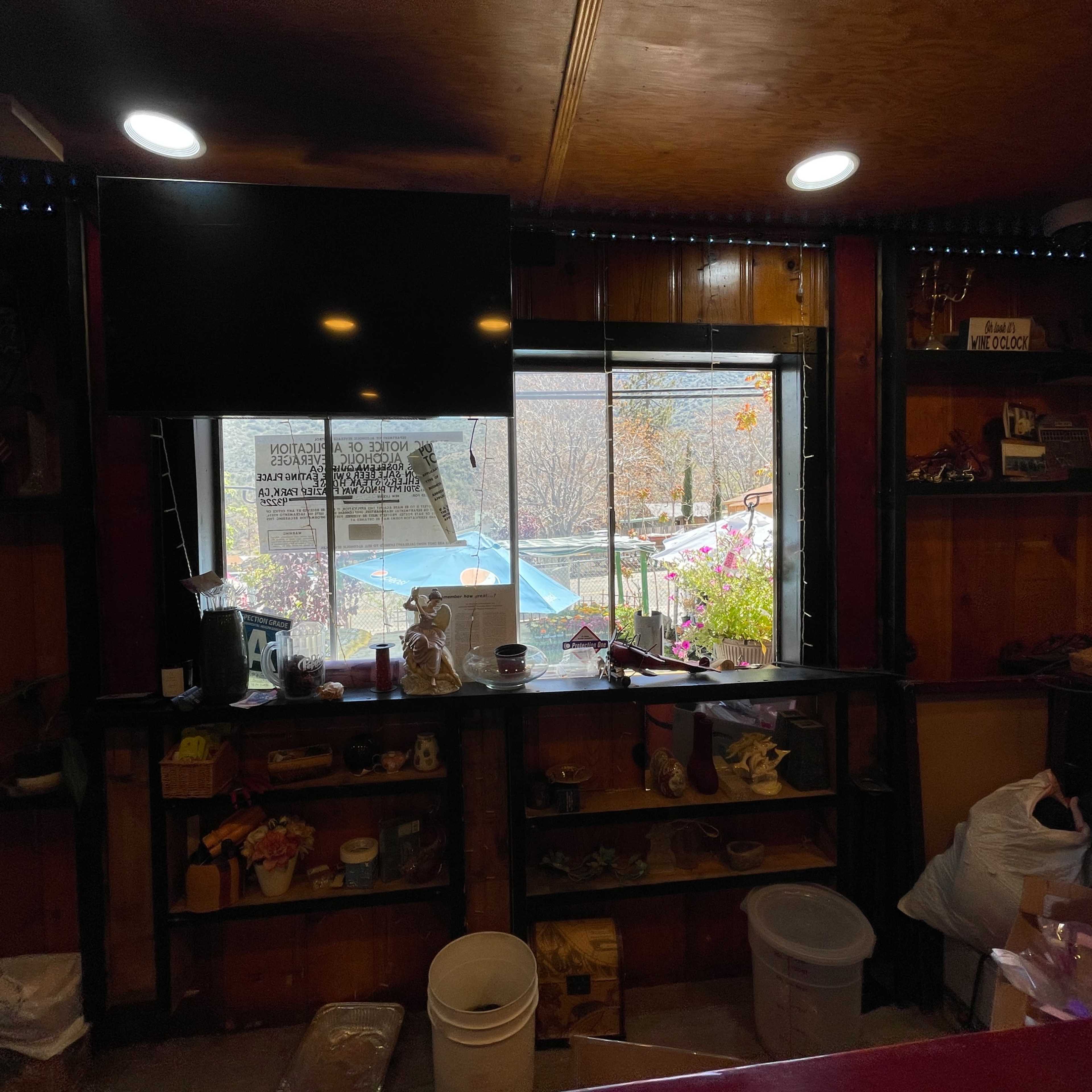 A wooden counter with various items displayed, overlooking a window that frames an outdoor scene with plants and a blue pool.