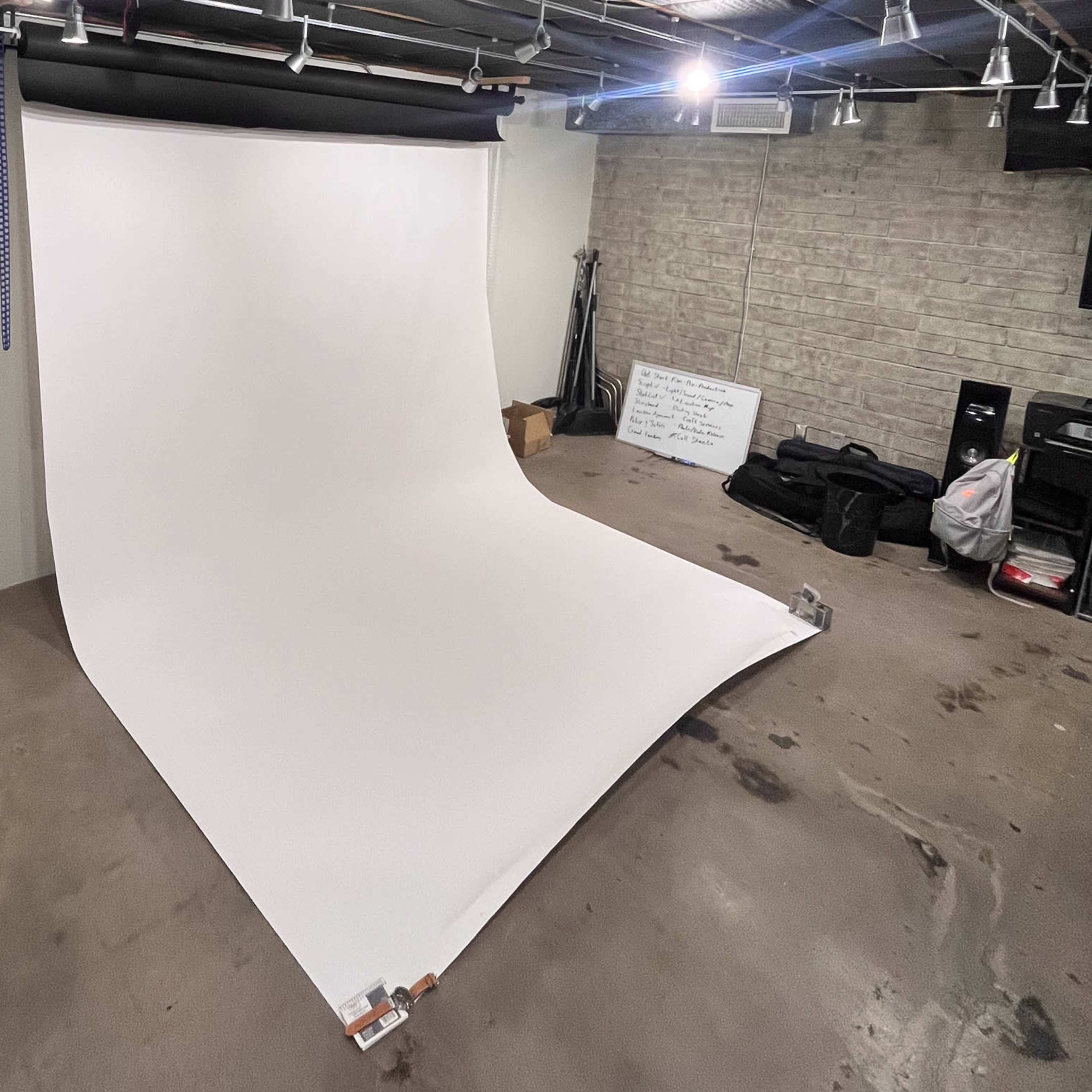 A smooth, white backdrop is set up in a dimly lit room with concrete flooring and various equipment in the background.