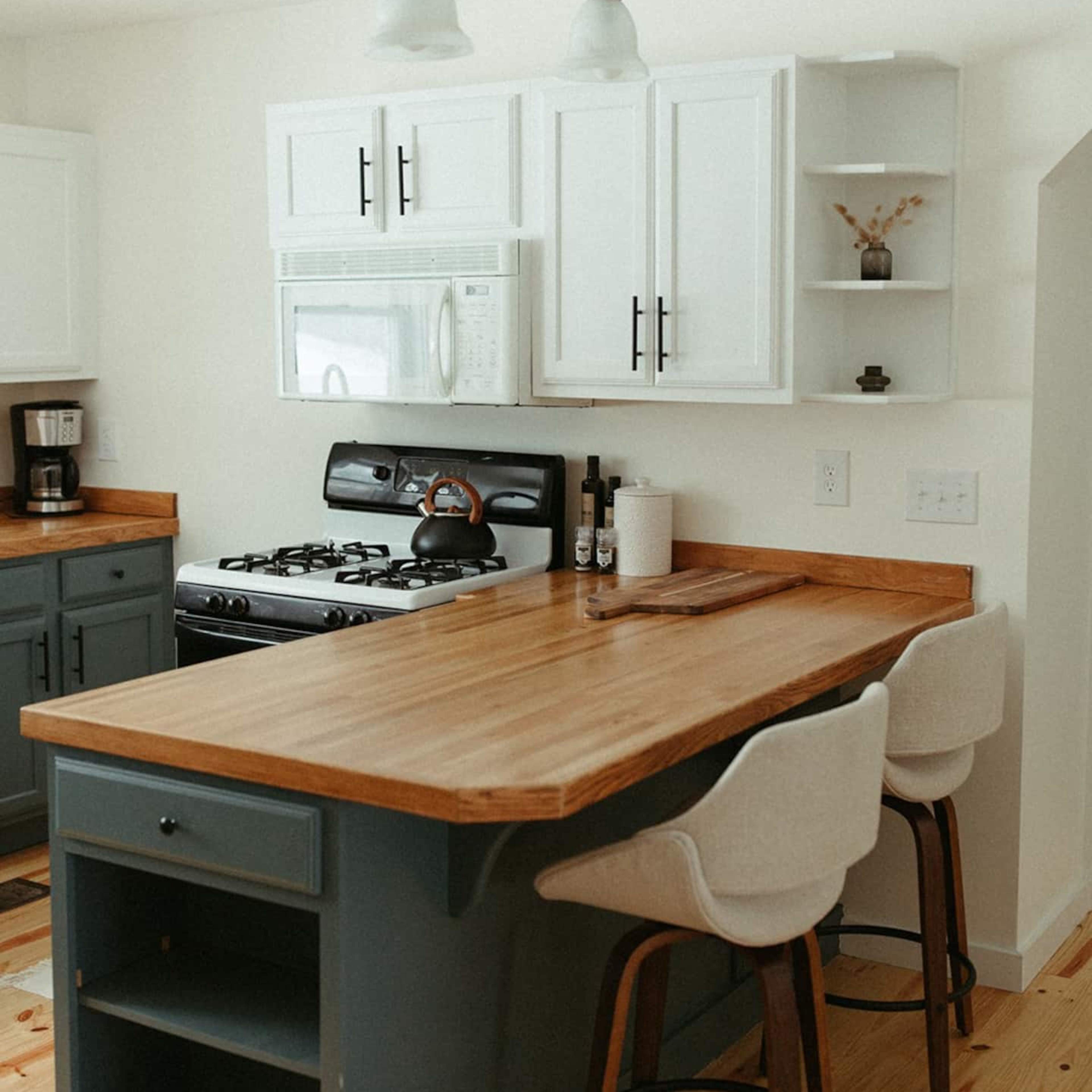 The kitchen features a wooden countertop island with bar stools, a gas stove, and white cabinetry with a minimalist design.