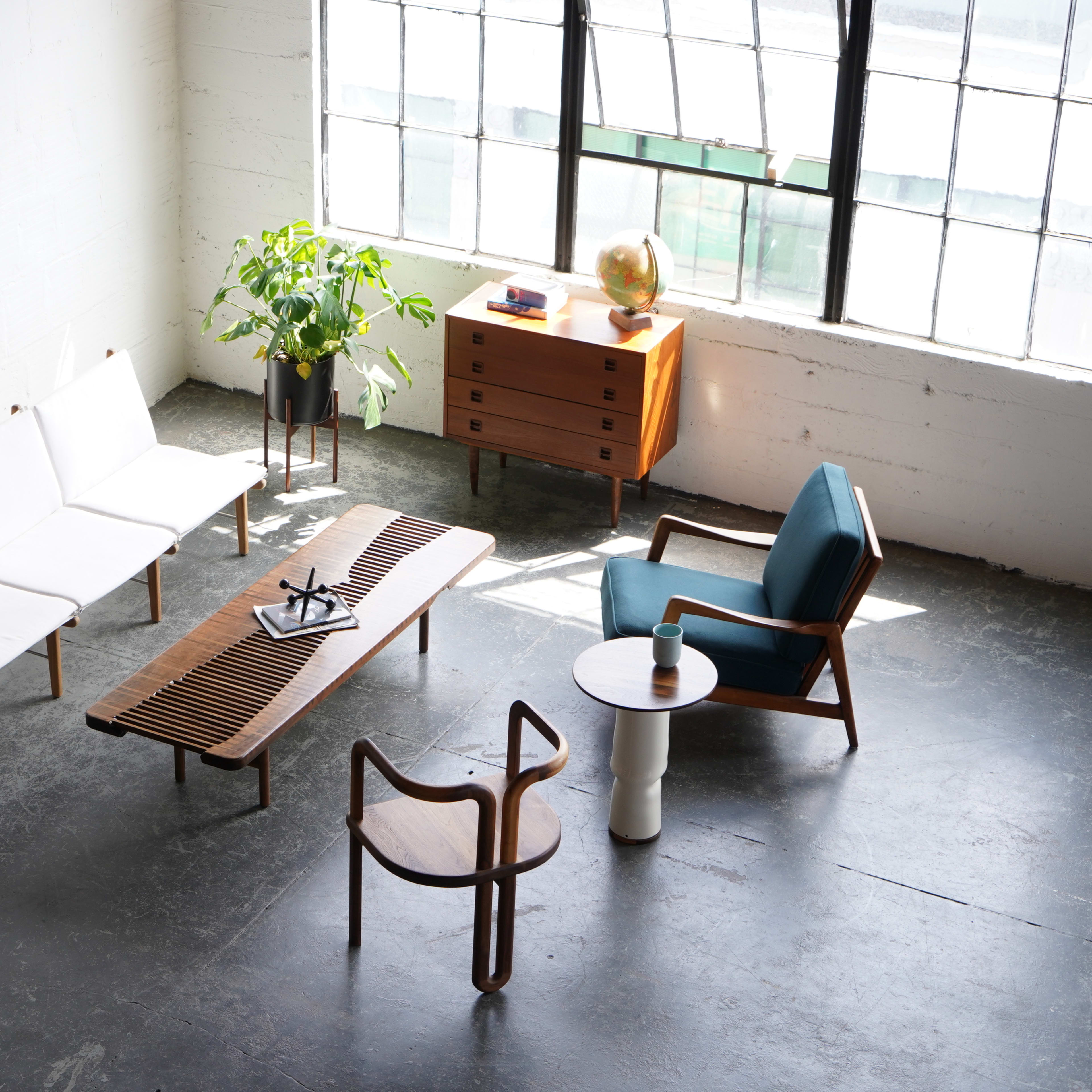 The scene features a modern living room with two sofas, a wooden coffee table, a small side table, a plant, a globe, and a storage cabinet arranged around a large window.