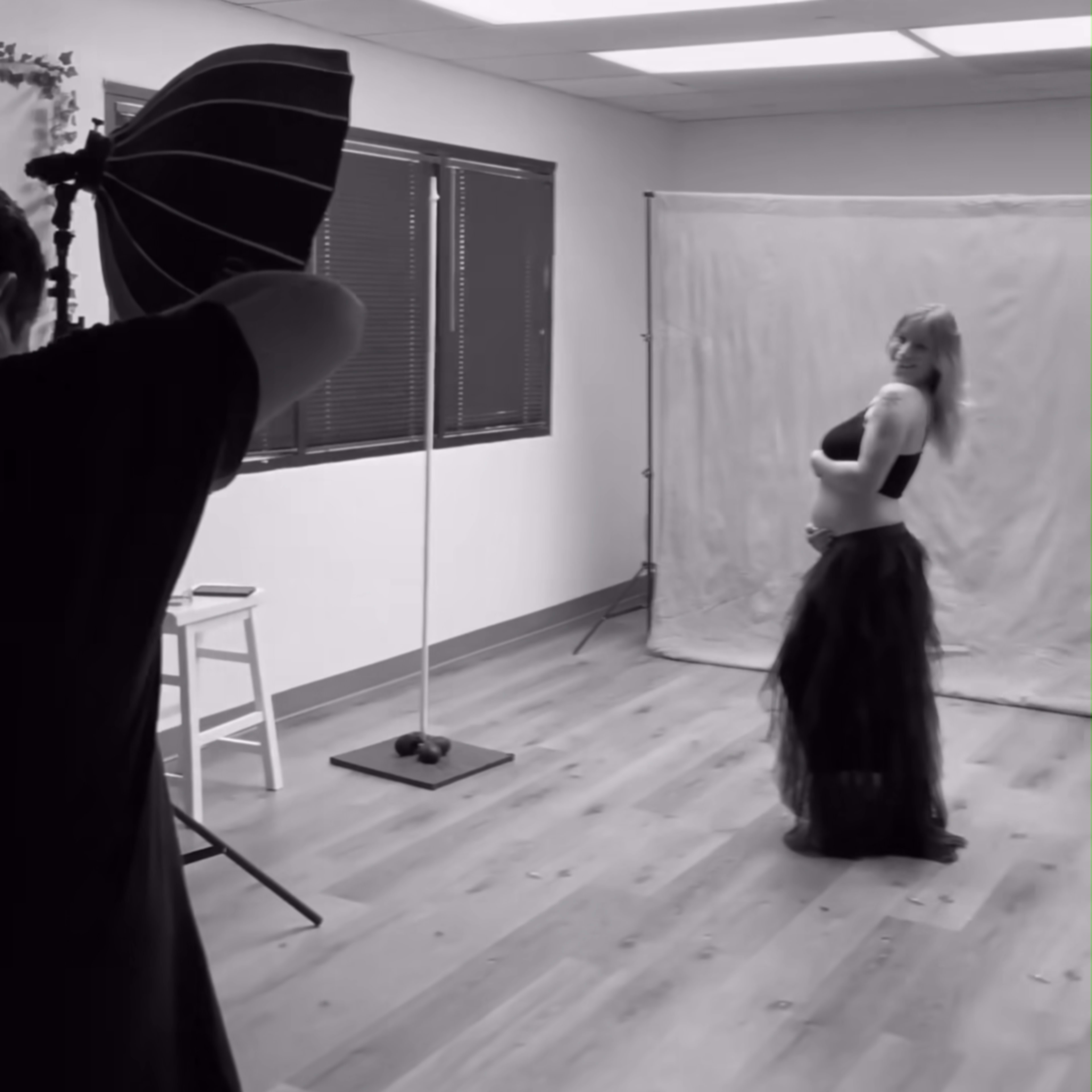 A photographer captures a model in a studio setting while she poses in a black skirt against a backdrop.