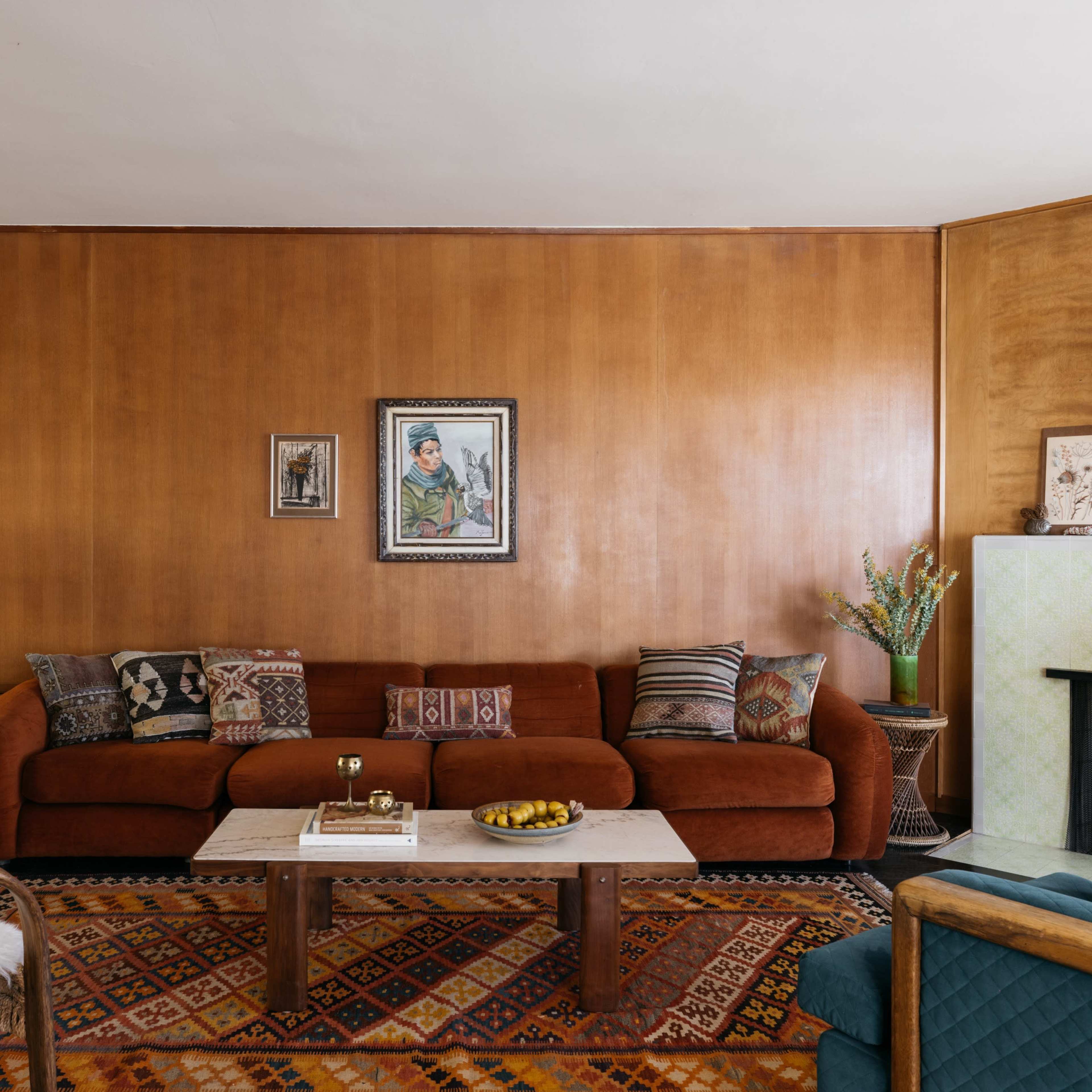A living room with a brown sofa, a patterned rug, and a wooden accent wall featuring artwork and decorative items.