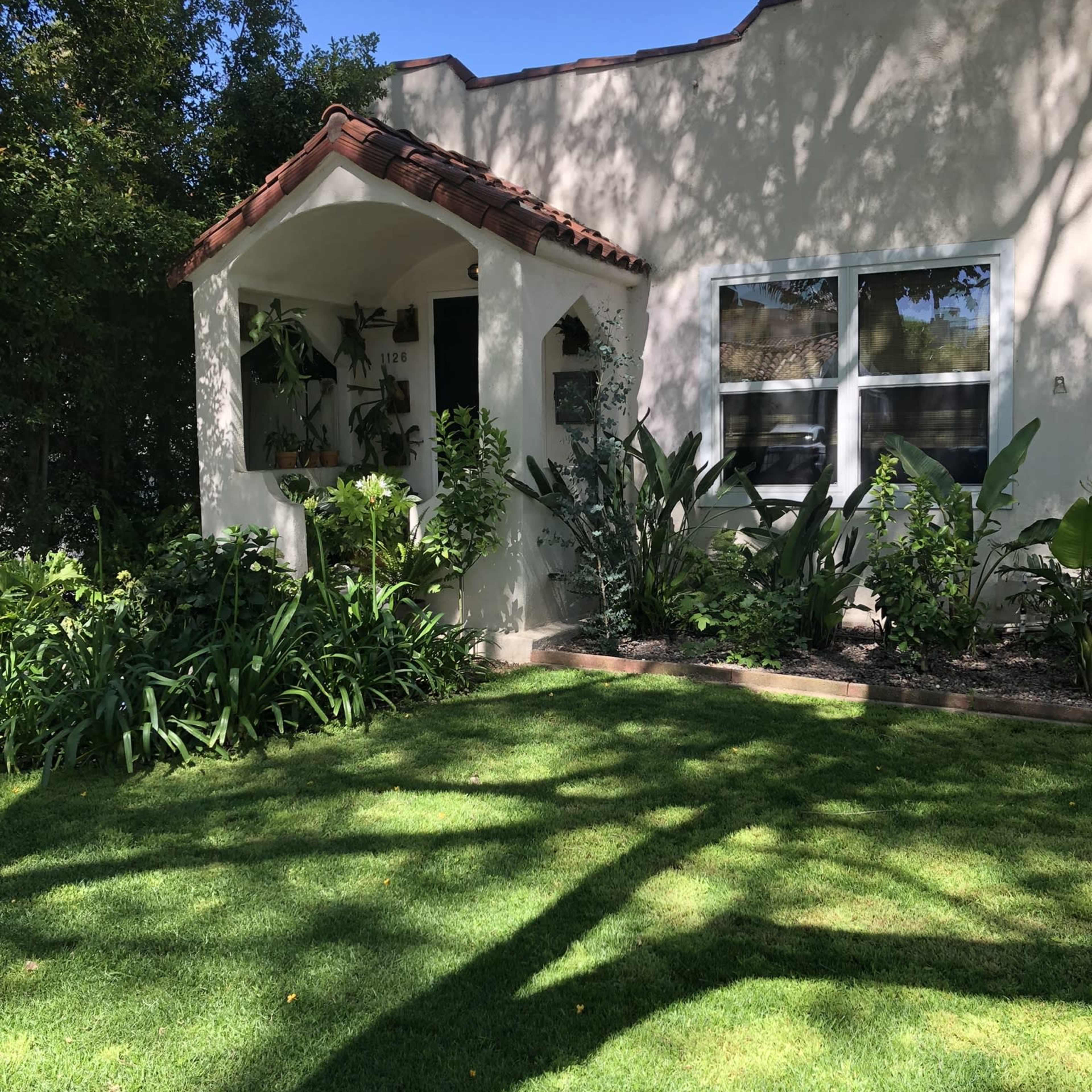 A house with a tiled roof and a front porch surrounded by lush greenery and well-maintained grass.