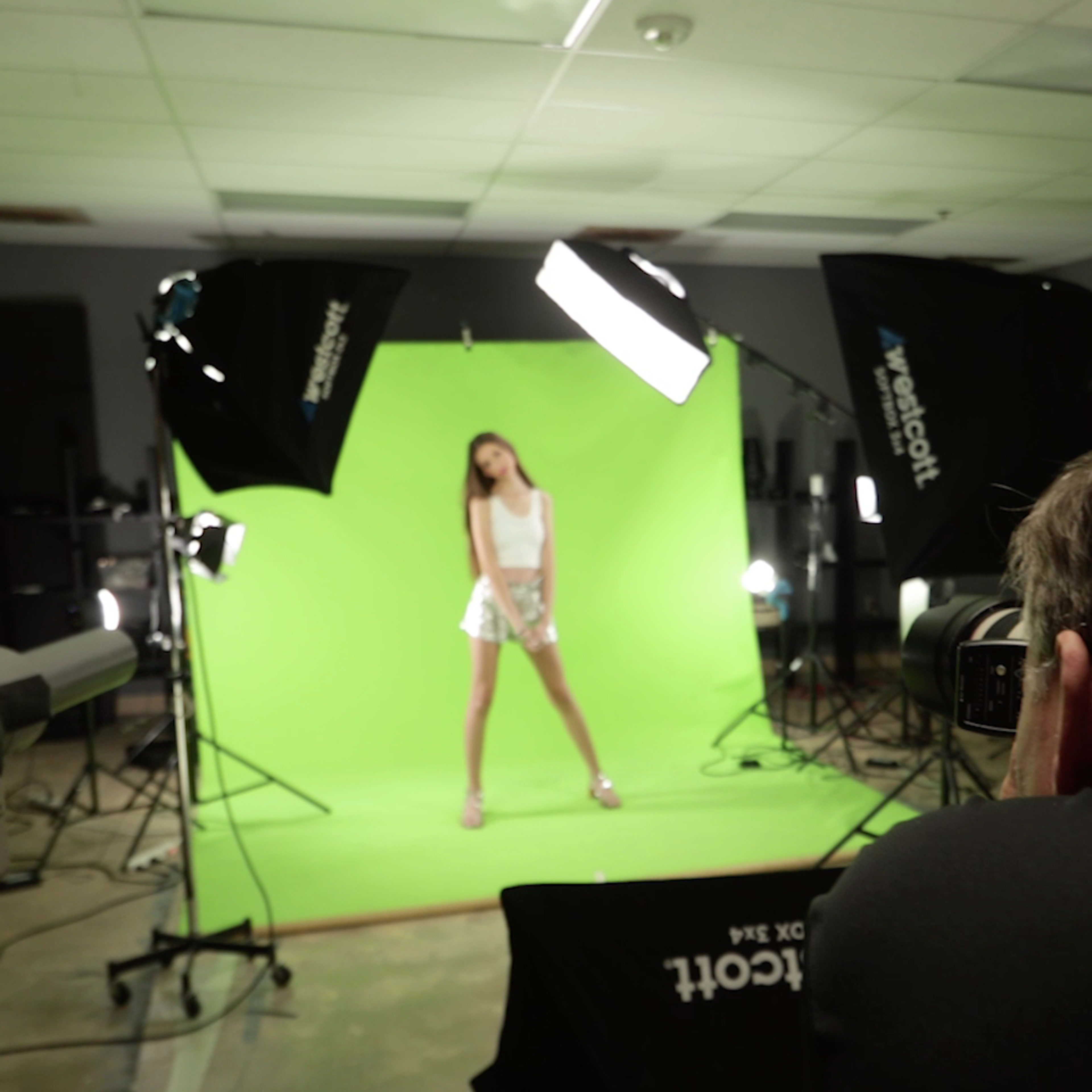 A photographer captures a model posing in front of a green screen surrounded by studio lighting equipment.