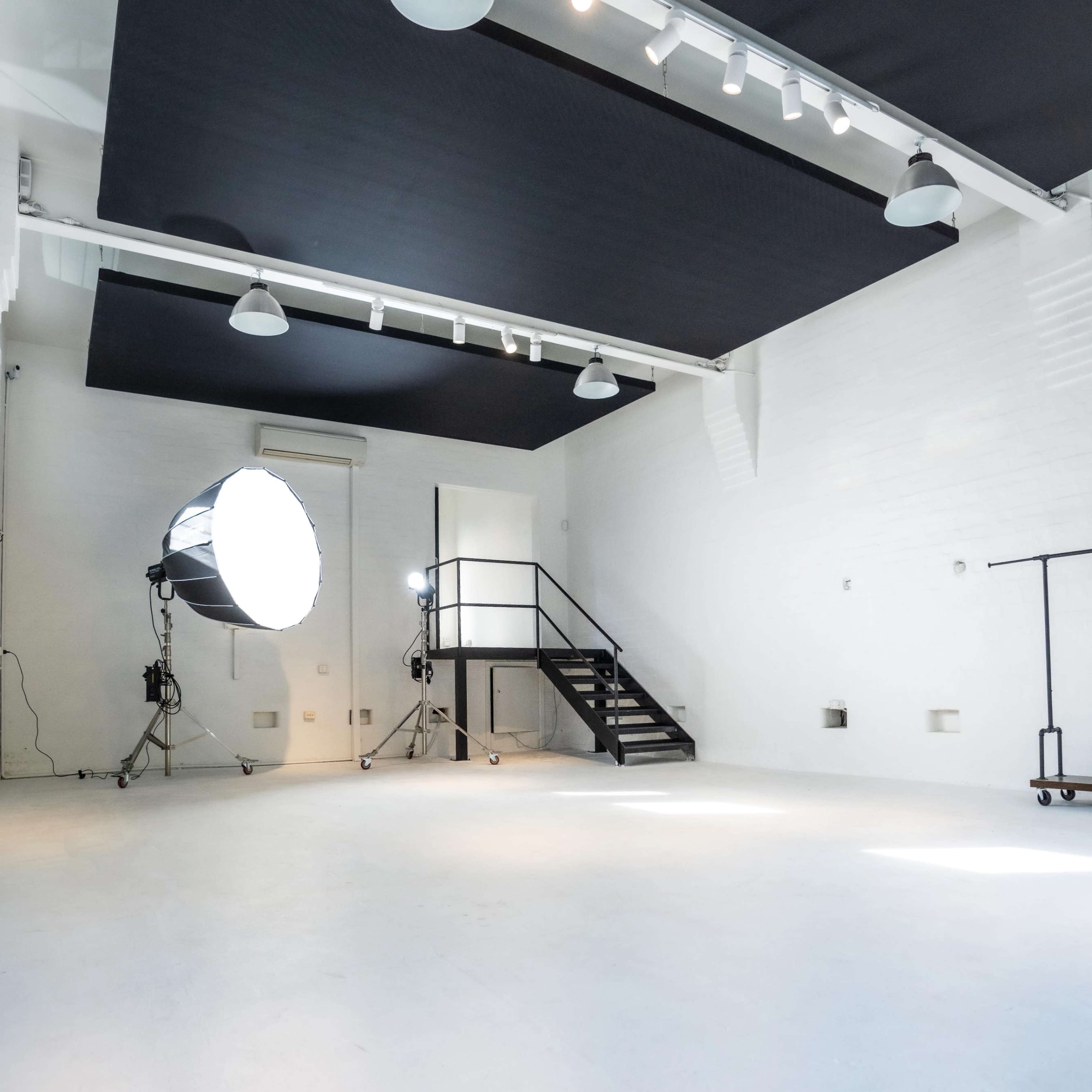 A spacious, well-lit photography studio with a staircase and lighting equipment set up.