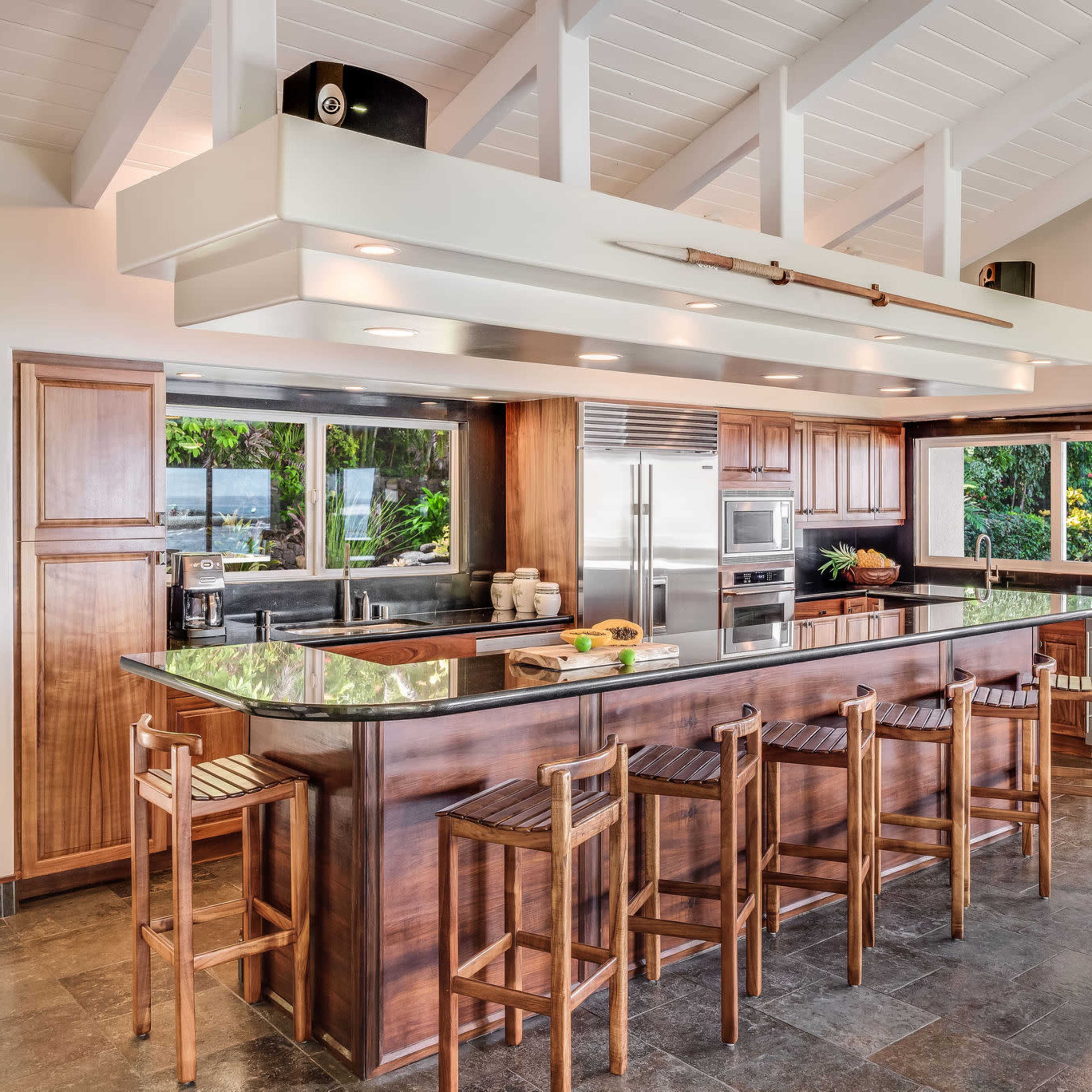 A modern kitchen with a large island, bar seating, and windows that overlook a garden.