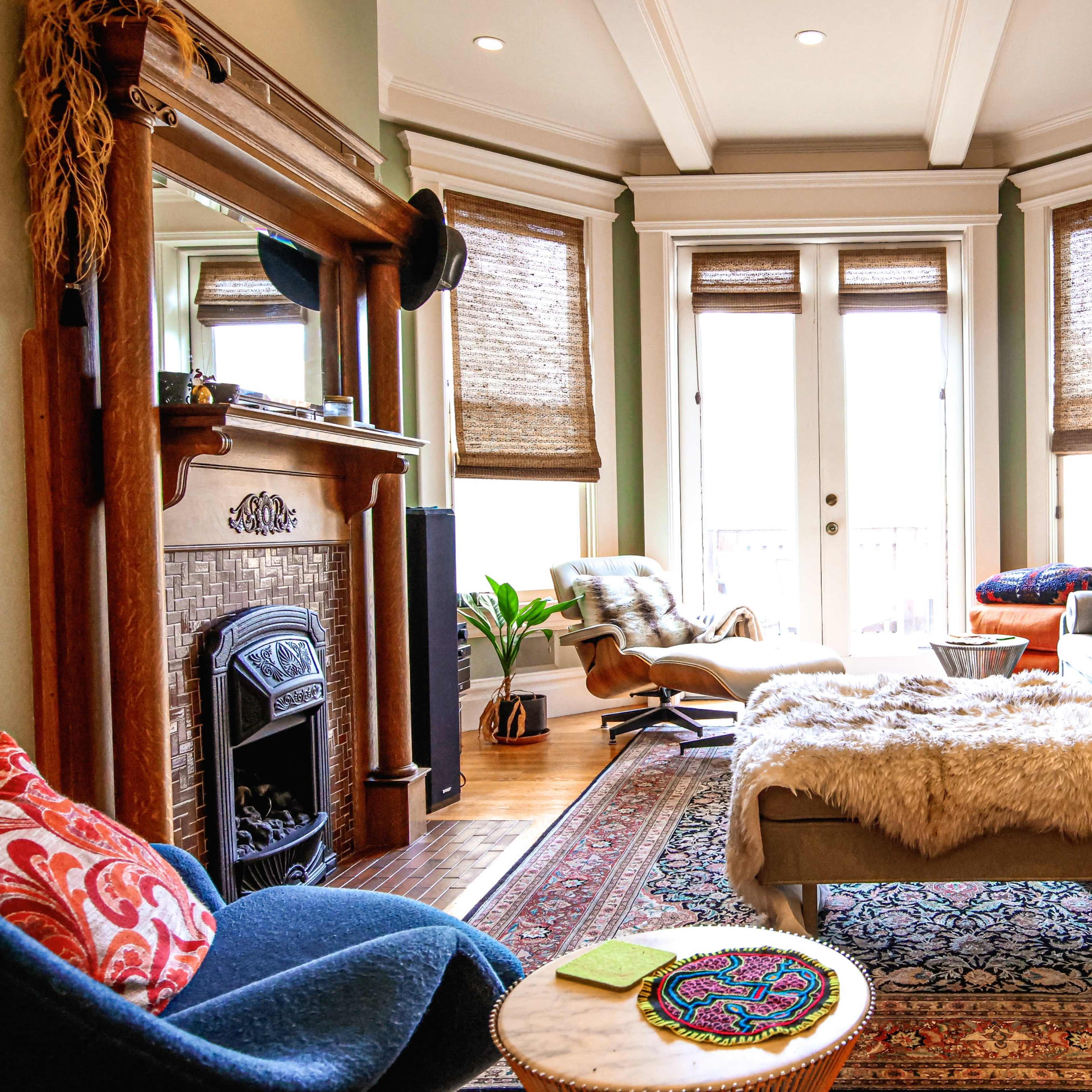 The living room features a cozy seating arrangement with a light-colored sofa, an armchair, a patterned rug, and large windows letting in natural light.