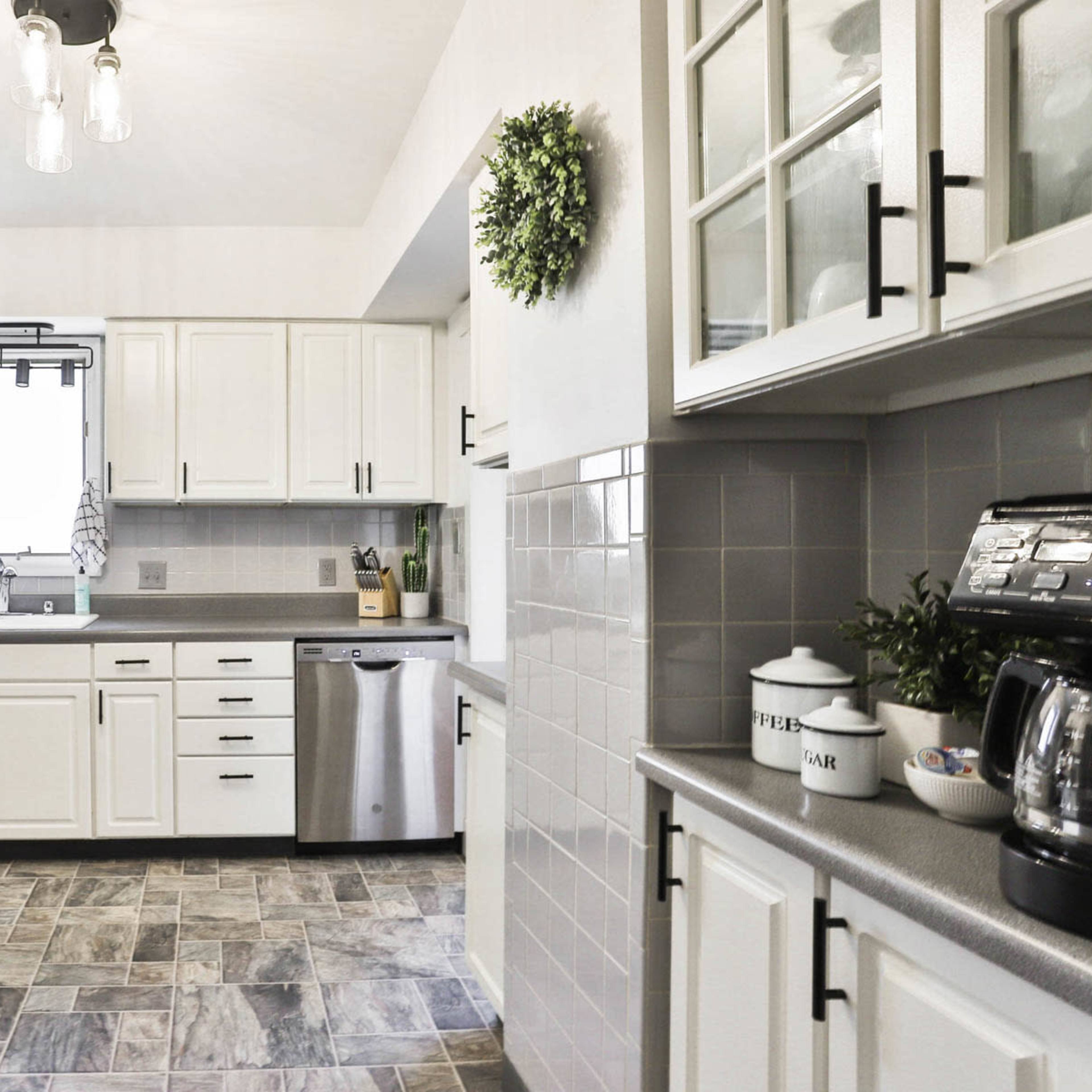 A modern kitchen with white cabinets, stainless steel appliances, and gray tiled flooring.