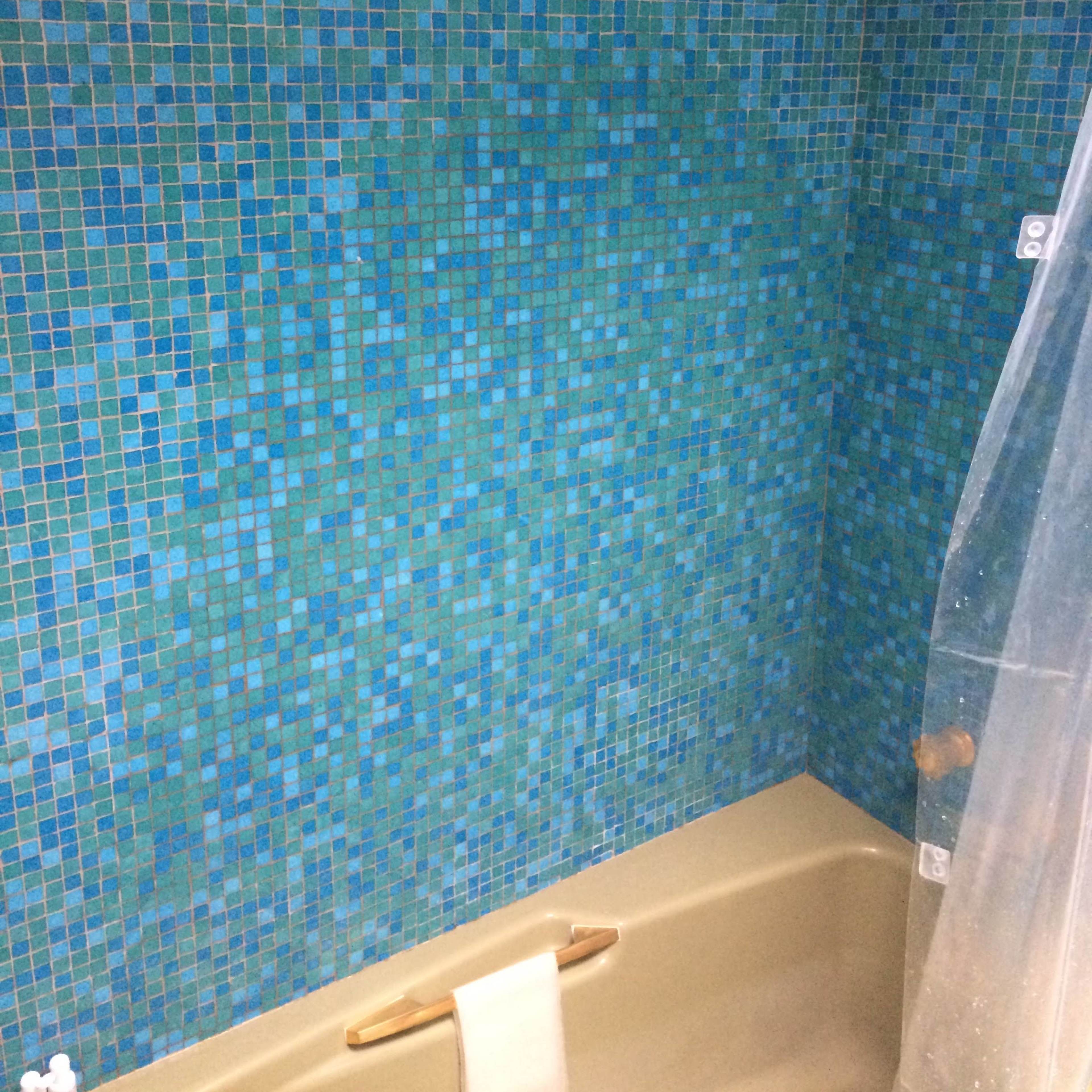 A bathroom wall covered in a mosaic of blue and turquoise tiles, with a tan bathtub in the foreground.