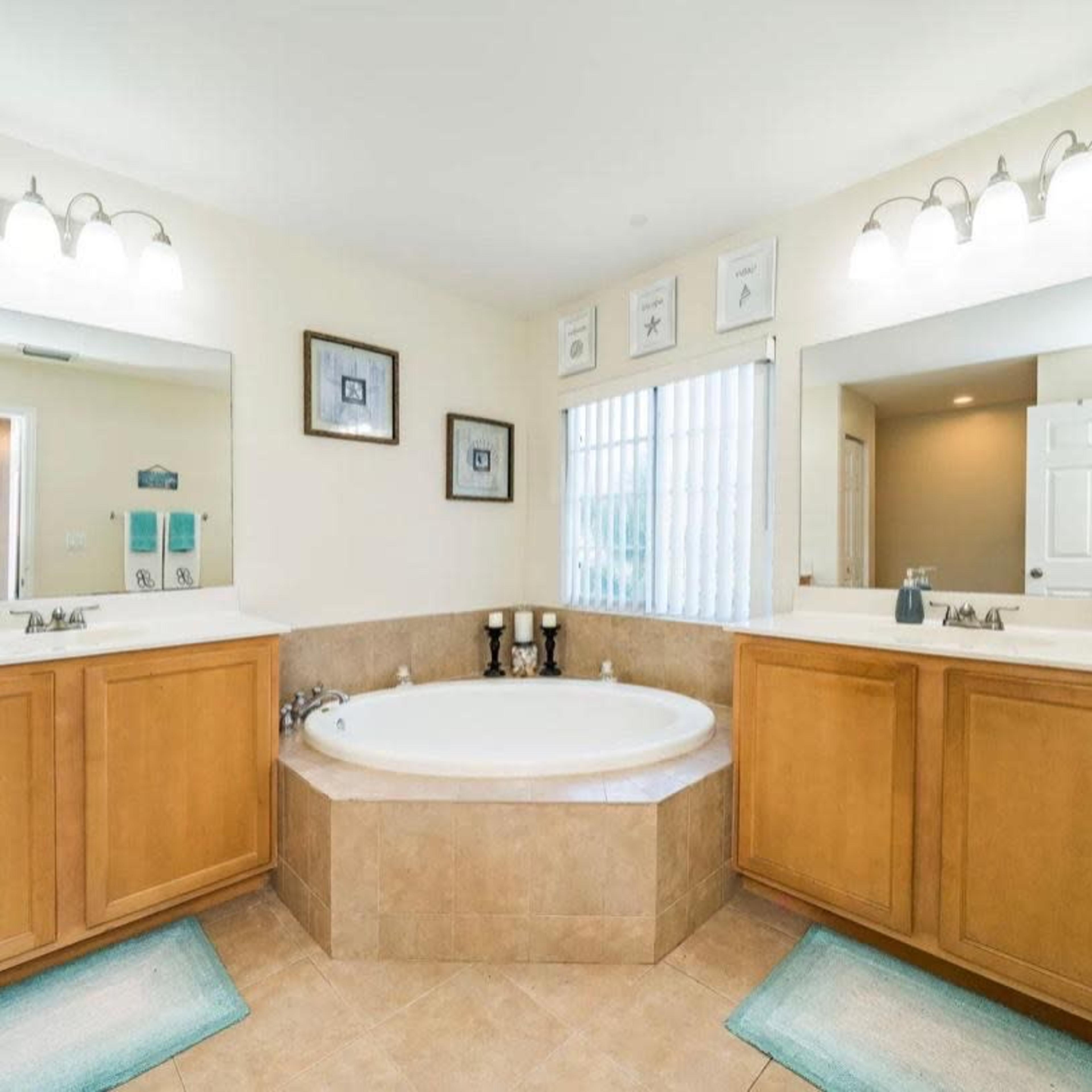 A spacious bathroom featuring a freestanding bathtub, dual sinks with wooden cabinetry, and two large mirrors.
