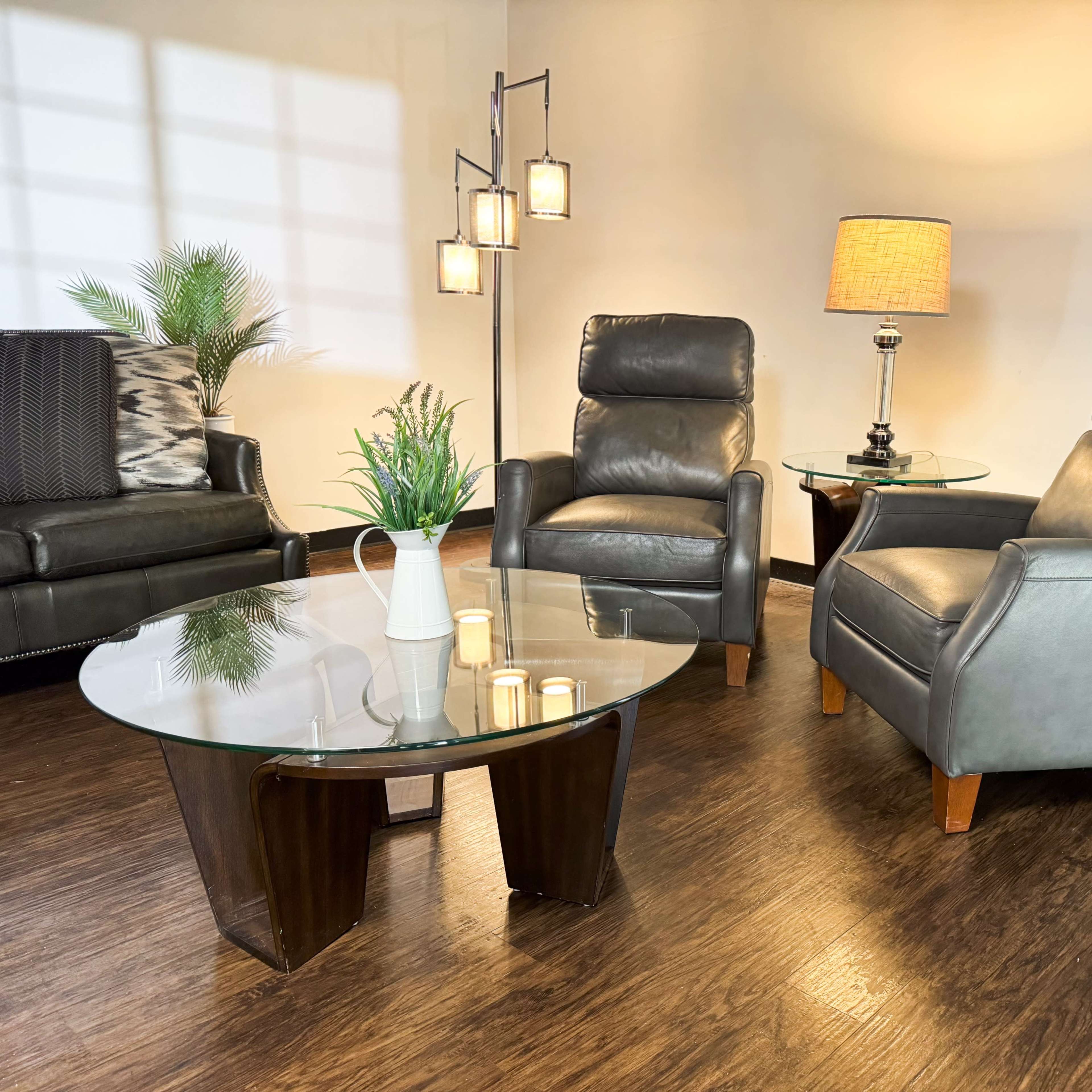 A cozy living room setting featuring two leather armchairs, a glass coffee table, a lamp, and decorative plants.