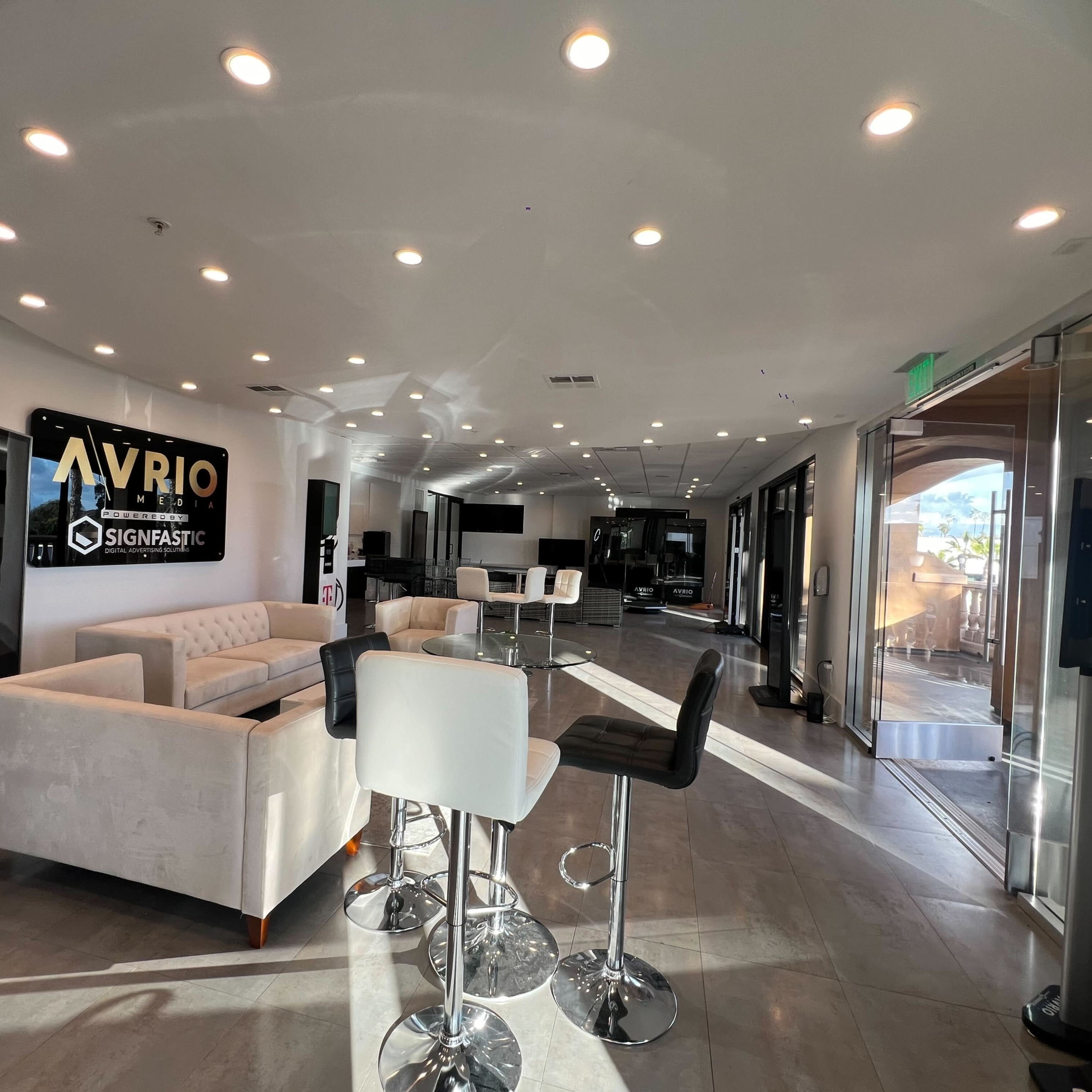 A modern open space with a seating area featuring a white sofa and bar stools, illuminated by circular ceiling lights.