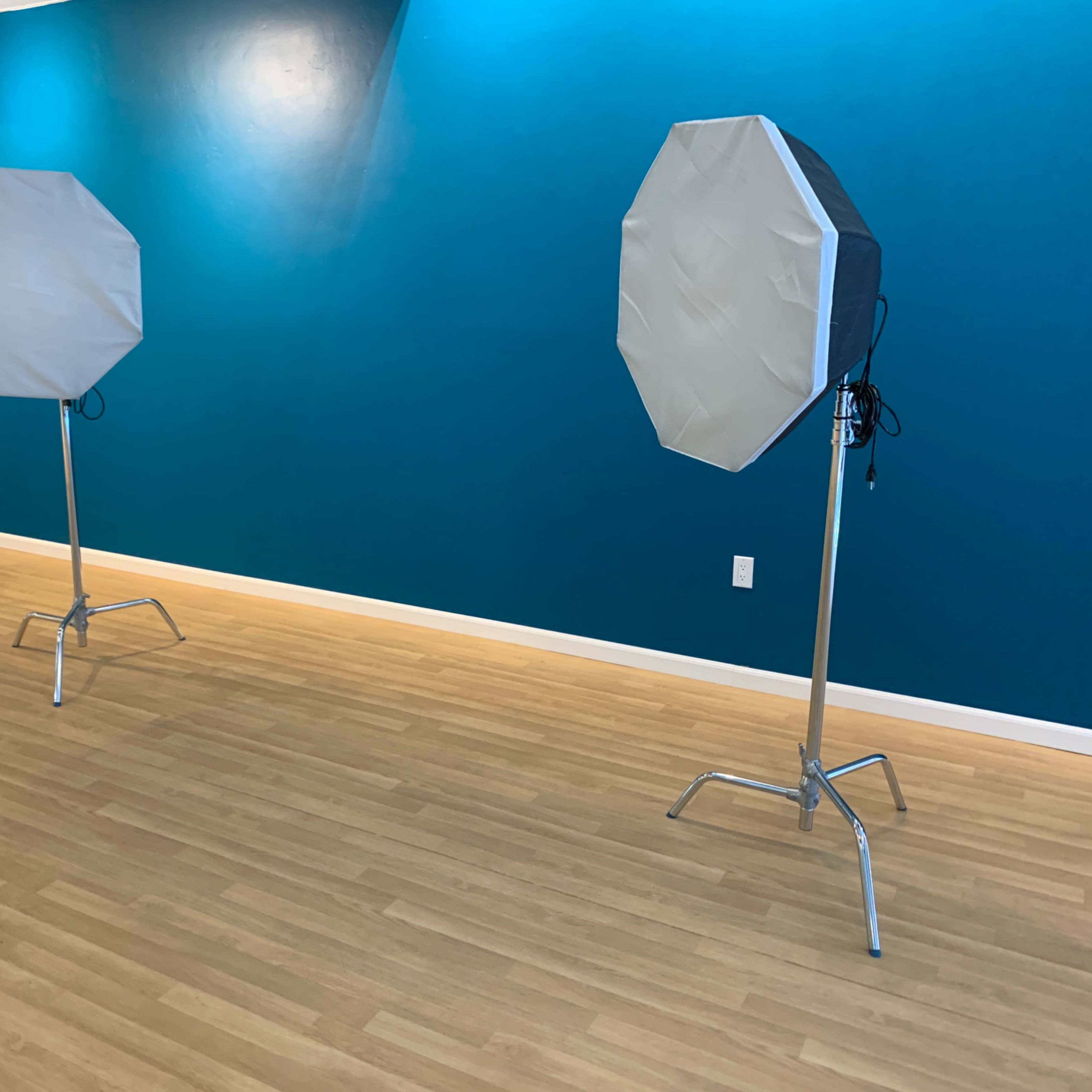 Two octagonal softboxes on stands are positioned in a room with a blue wall and wooden flooring.