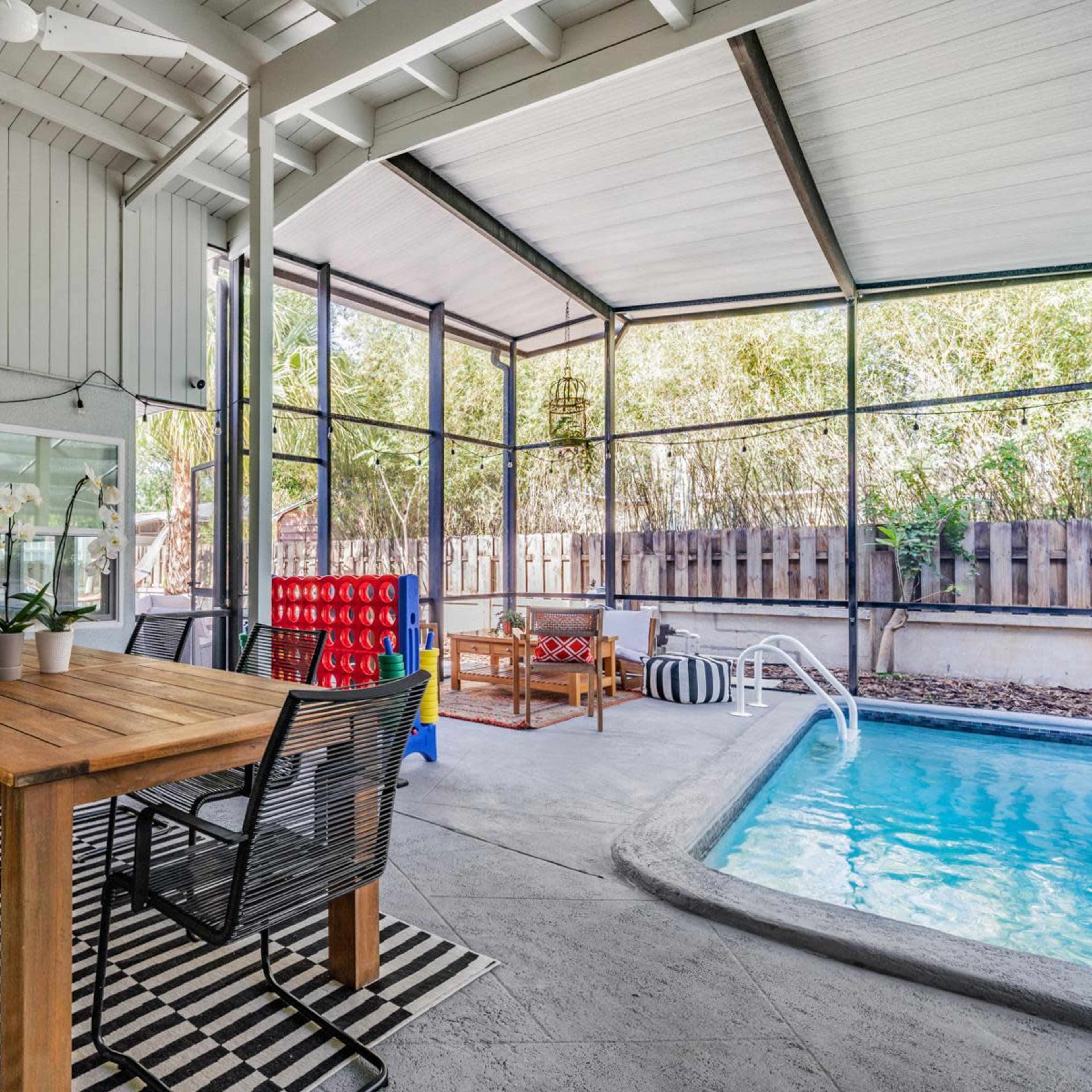 A screened-in patio area with a dining table, chairs, and a swimming pool.