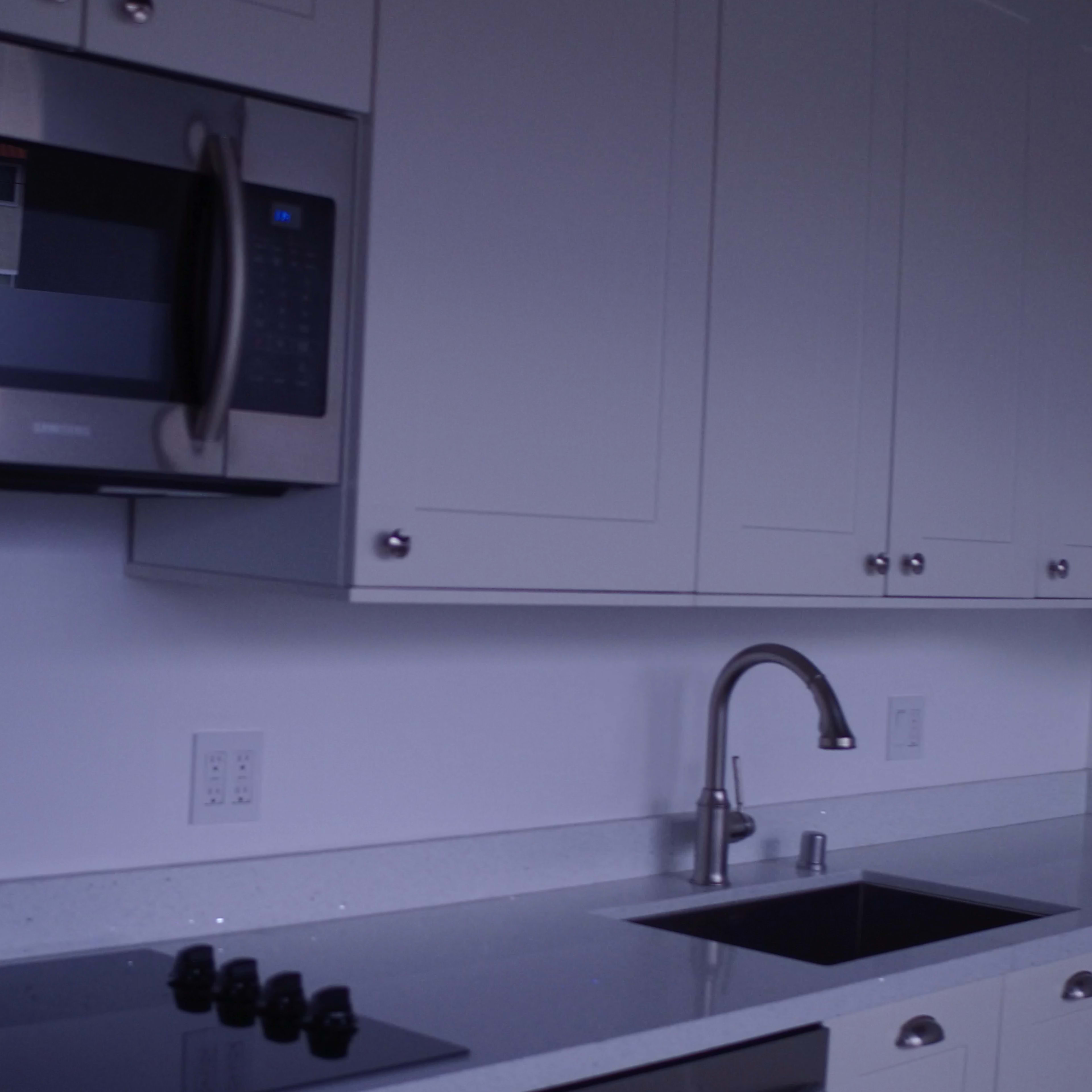 The kitchen features white cabinetry, a stainless steel microwave, a sleek countertop, and a single basin sink.
