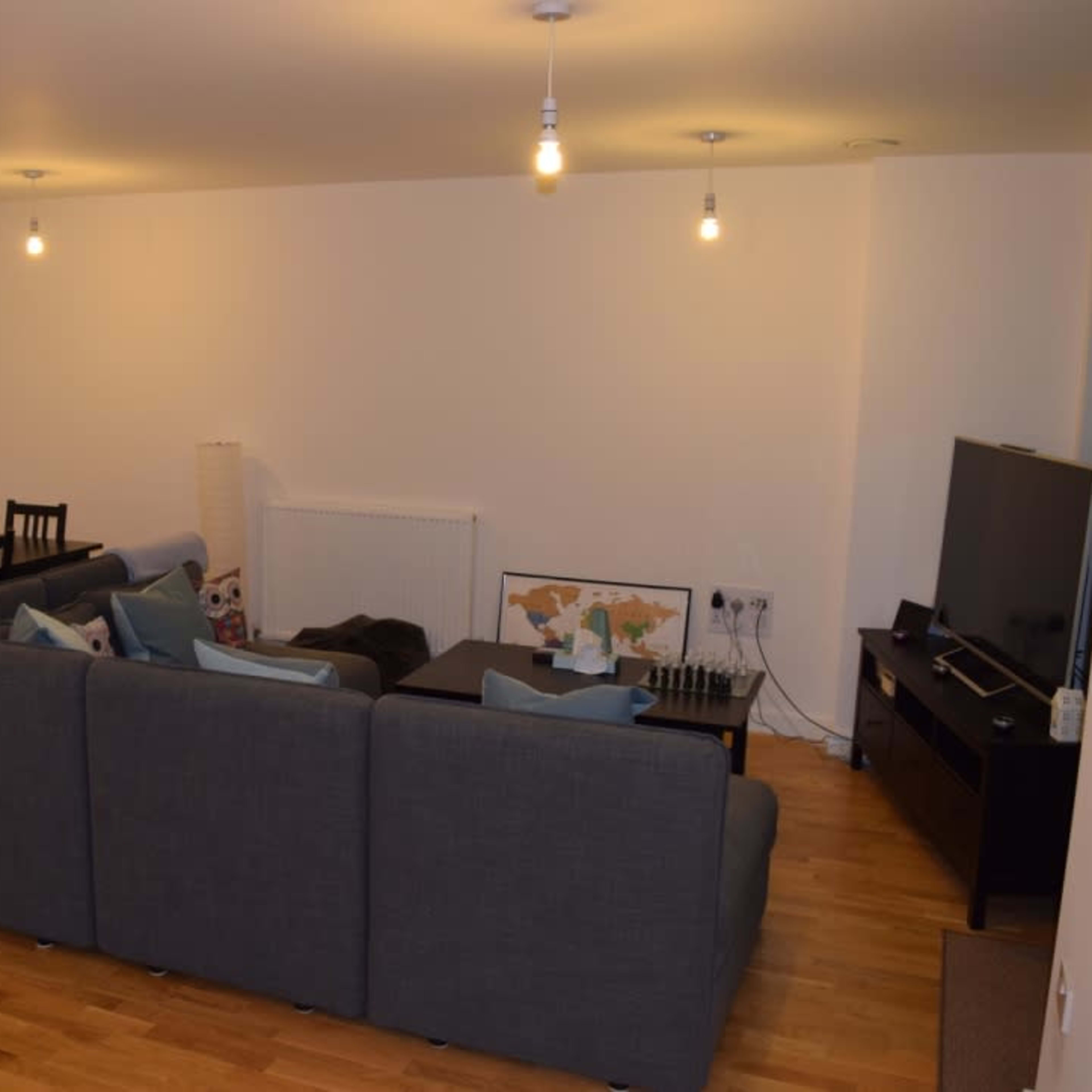 A modern living space with a dark gray sectional sofa, a dining area with a table and chairs, and a television on a low cabinet.