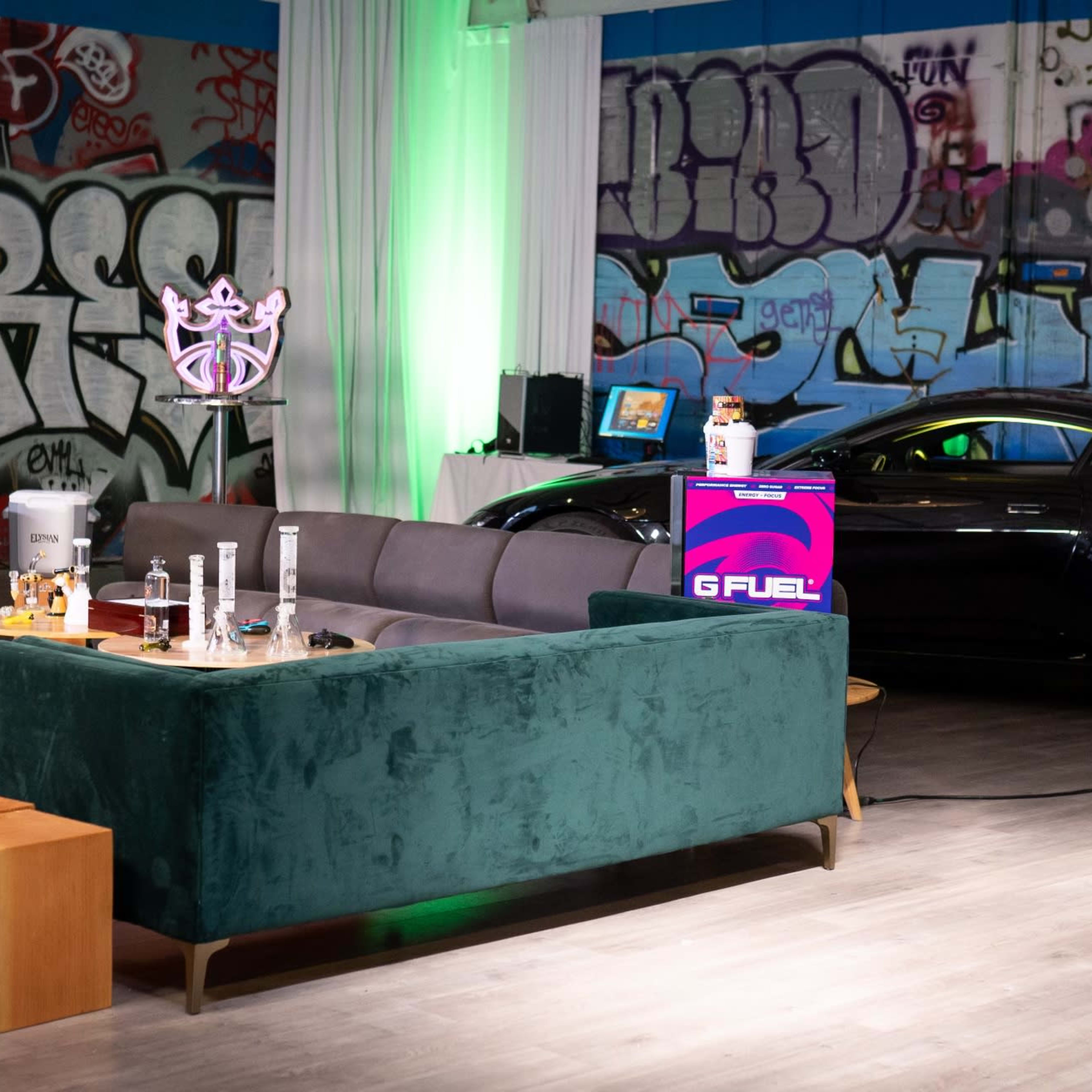 A modern lounge area with a green sofa, wooden tables, and colorful graffiti on the walls, alongside a sports car.