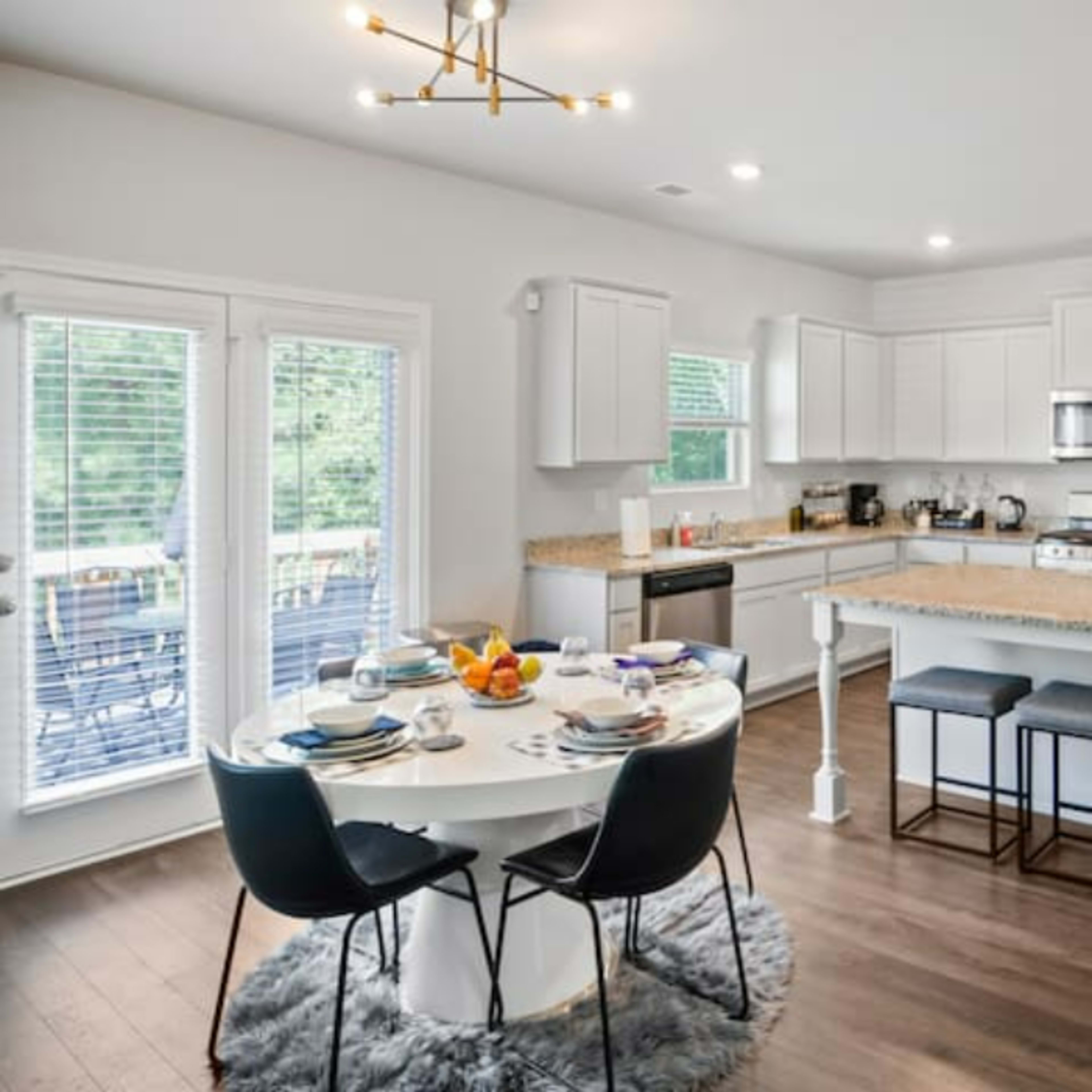 A modern kitchen with a circular dining table set for a meal, featuring a stainless steel refrigerator and white cabinetry.