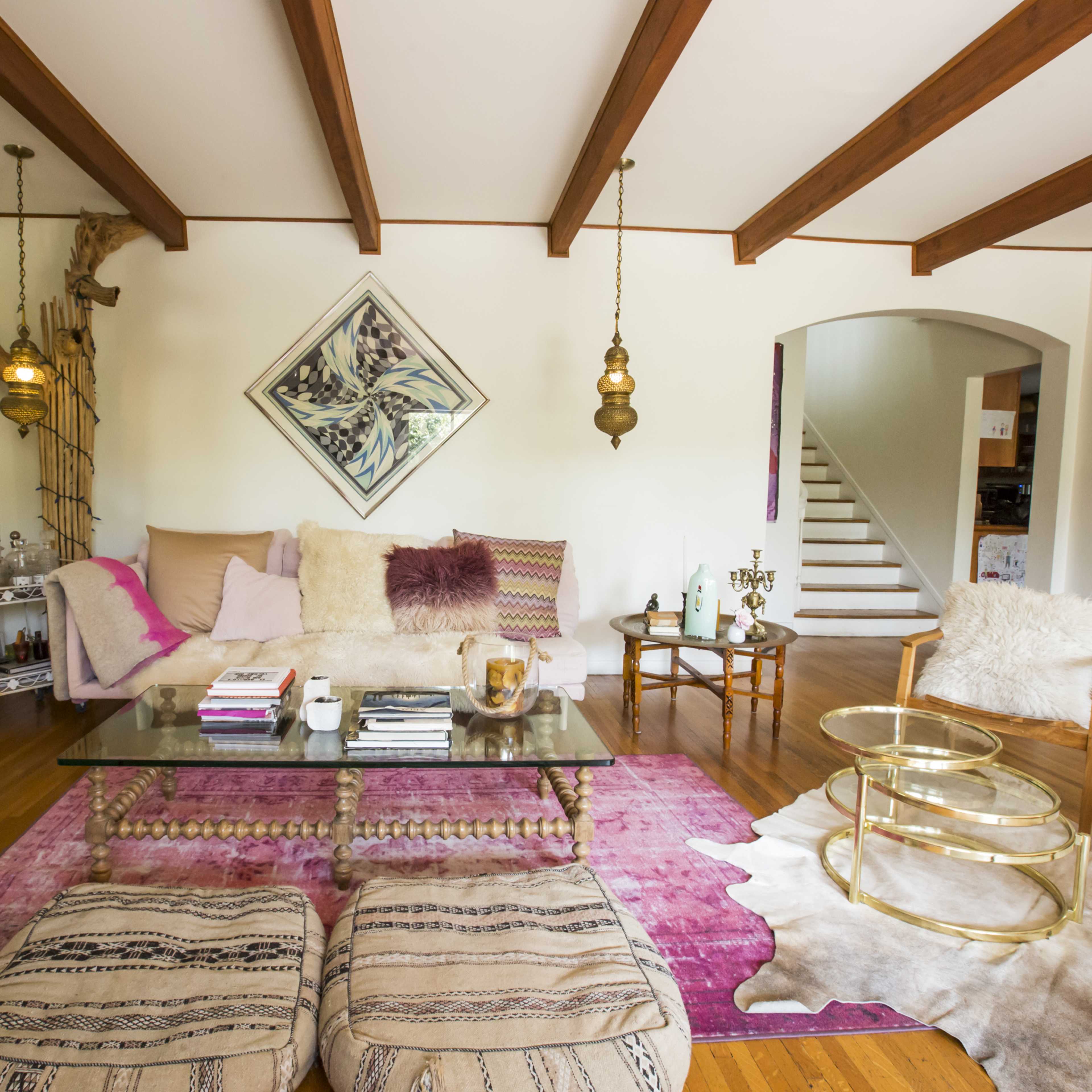 The living room features a cream sofa with purple and pink accents, a glass coffee table on a patterned rug, and wooden beams on the ceiling.