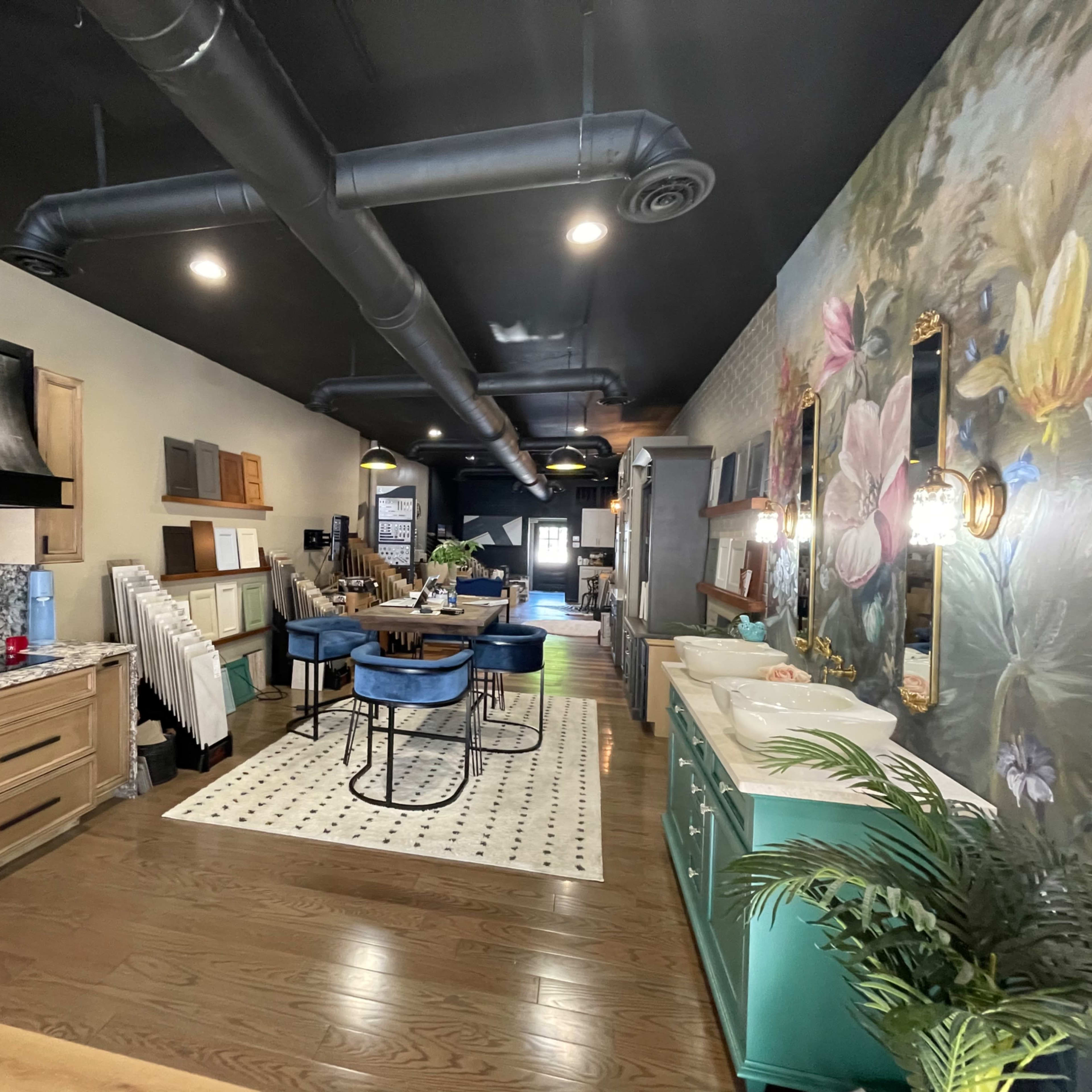 A modern kitchen and dining area with wooden cabinetry, a large table surrounded by blue chairs, and a wall adorned with a floral mural.