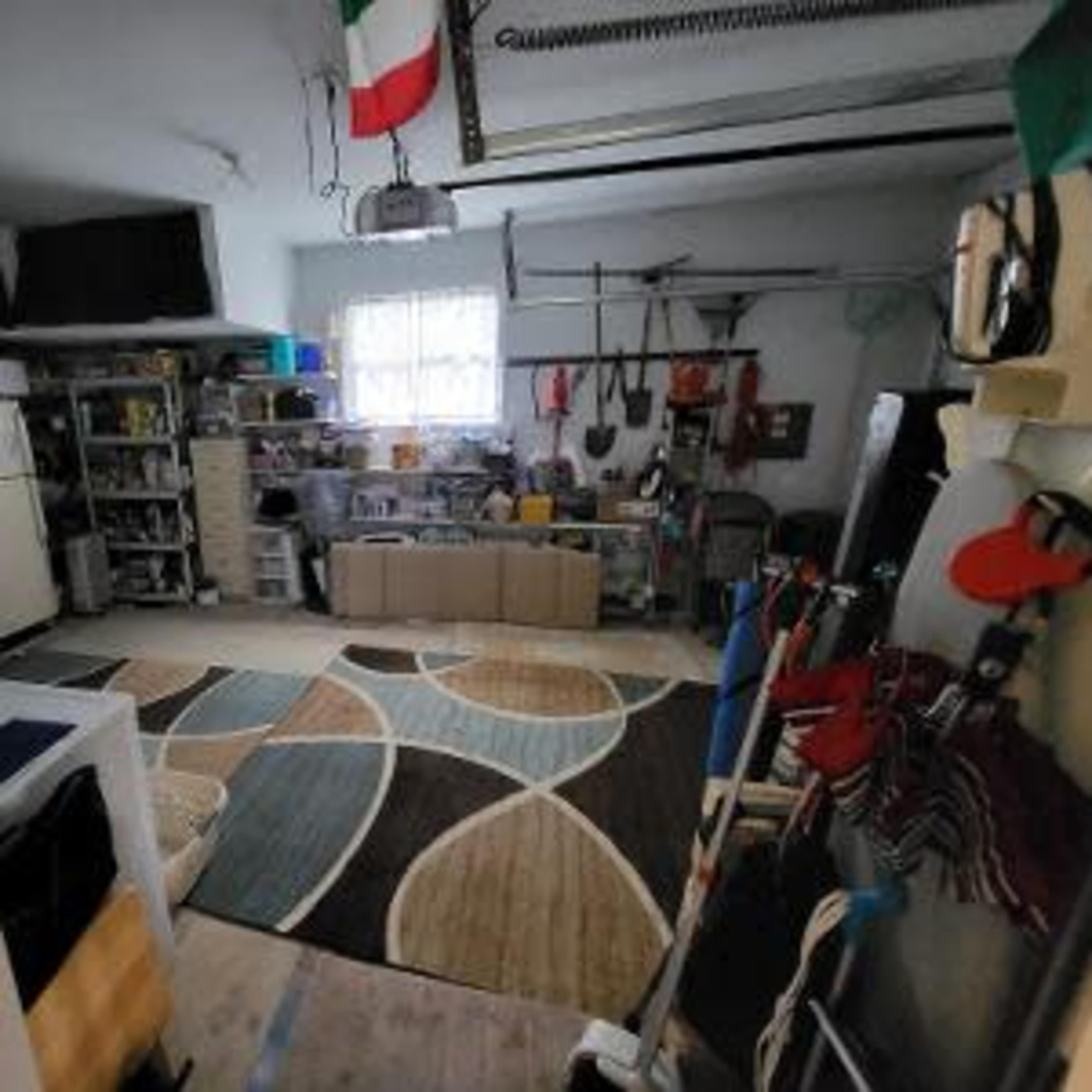 A garage space organized with shelving, tools, and a patterned rug on the floor.